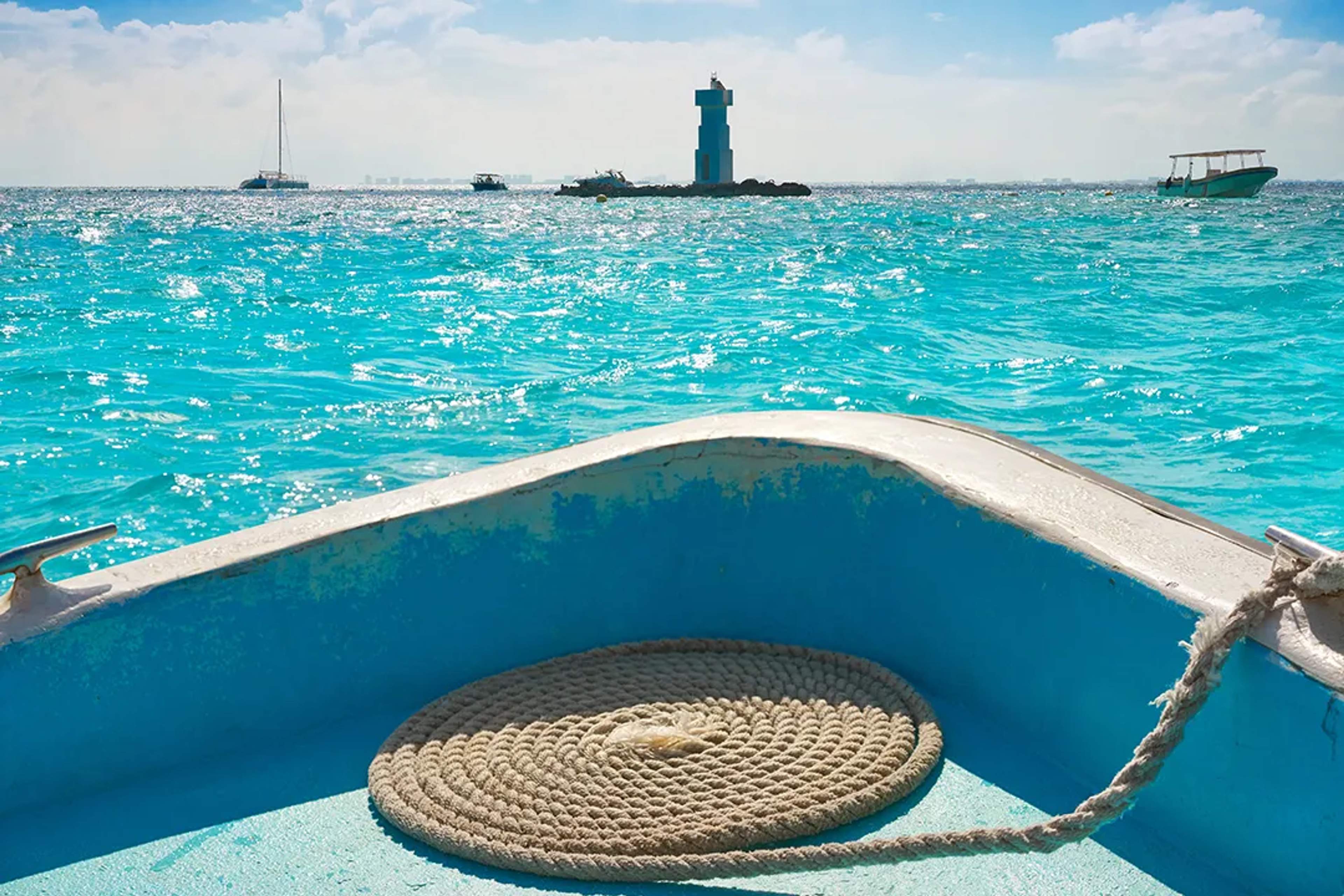 View from a boat over turquoise waters toward a lighthouse and distant sailboats.