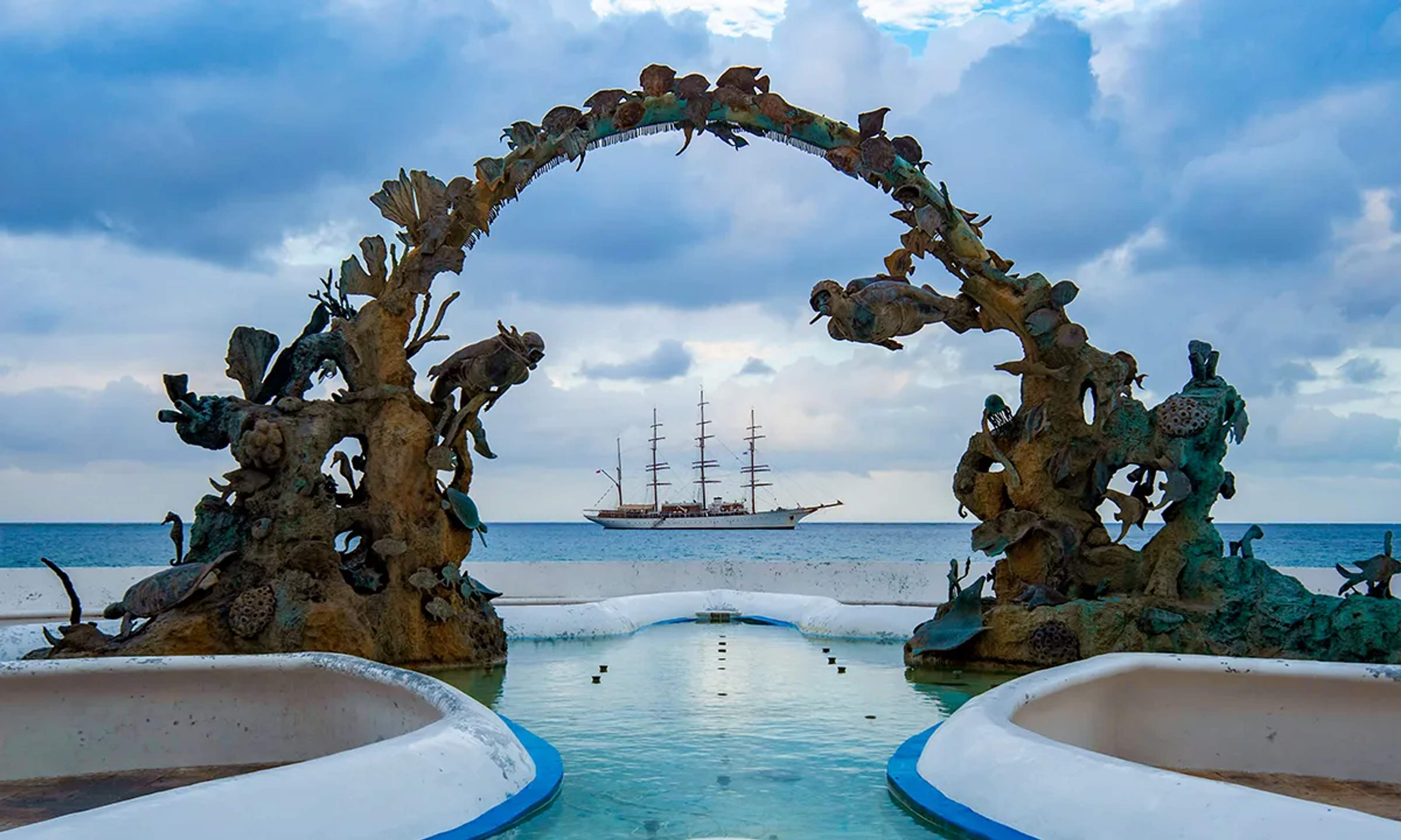 Arco escultórico en Cozumel enmarcando un velero sobre el mar Caribe, una mezcla de arte, historia y belleza natural.