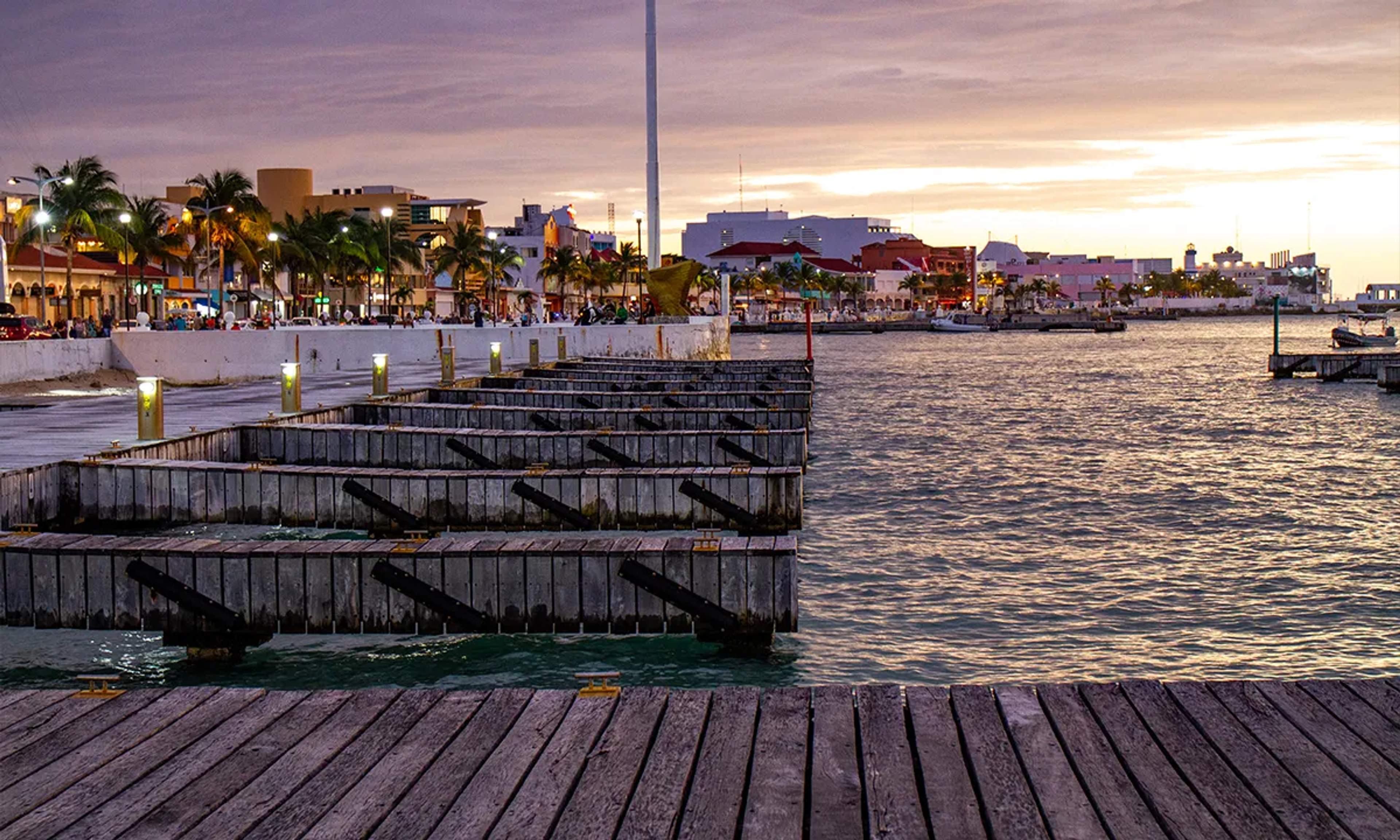 Atardecer en el malecón de Cozumel, con muelles de madera y luces que reflejan el encanto de la vida caribeña.