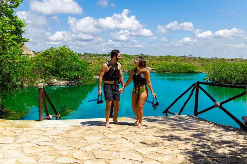 Couple walking by a turquoise lagoon with snorkel gear during a scenic eco adventure in Cancun