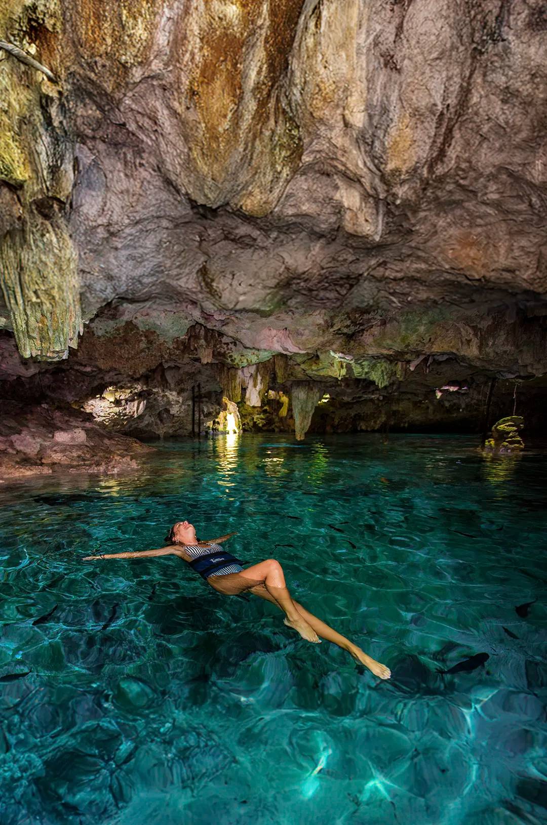 Mujer flotando en un cenote cerrado de aguas cristalinas.