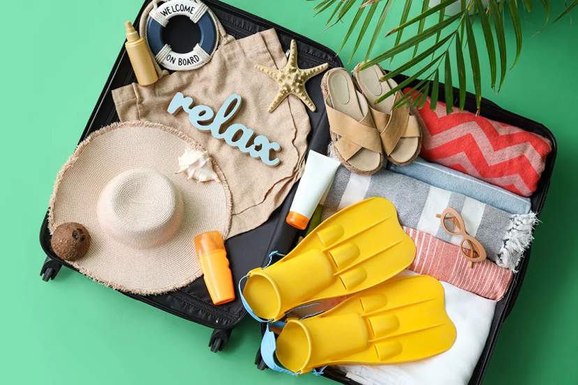 Open suitcase with beachwear, fins, hat, sandals, sunscreen, and travel essentials for a Cancun trip