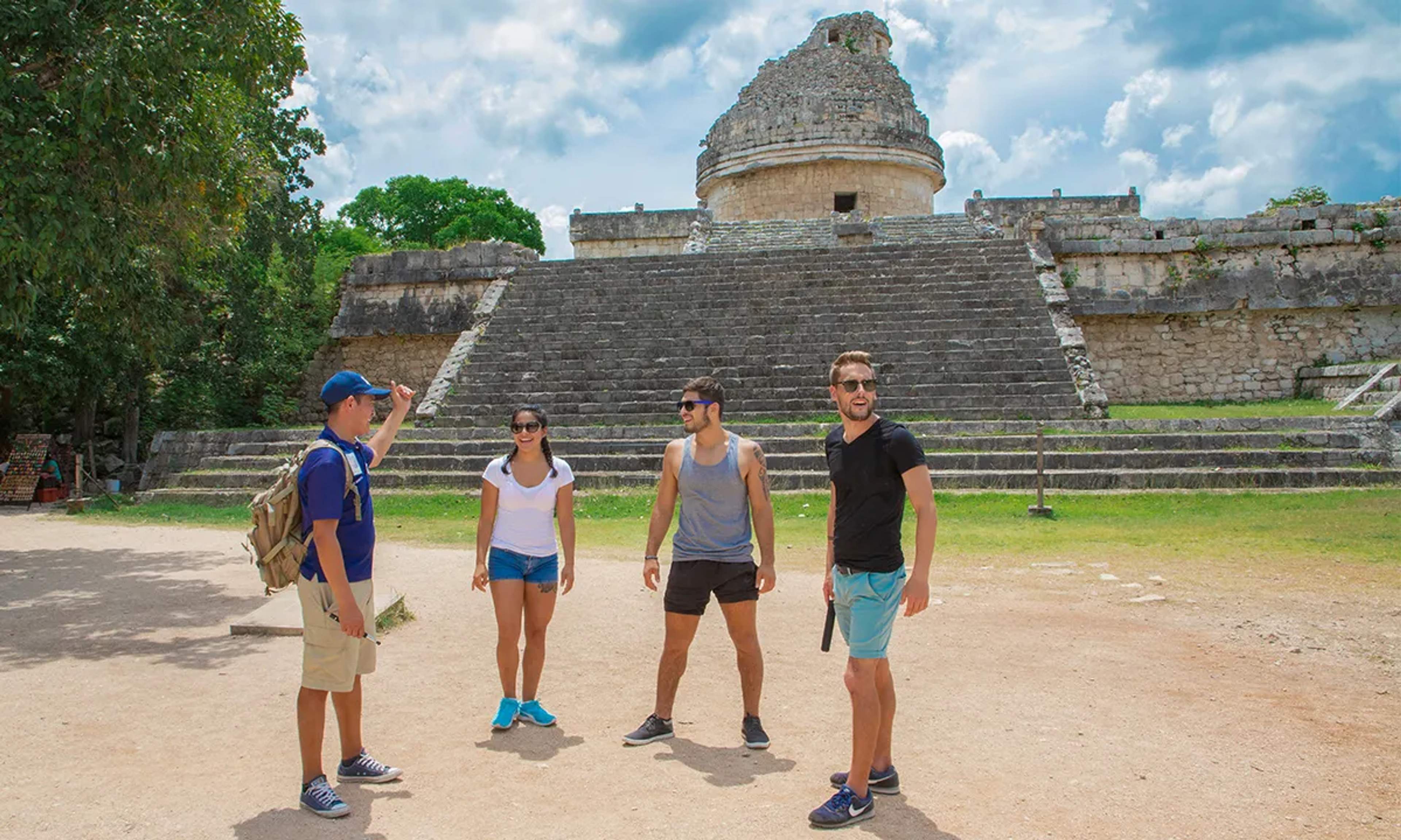 Grupo de turistas escuchando a un guía frente a una estructura en la zona arqueológica de Chichén Itzá.