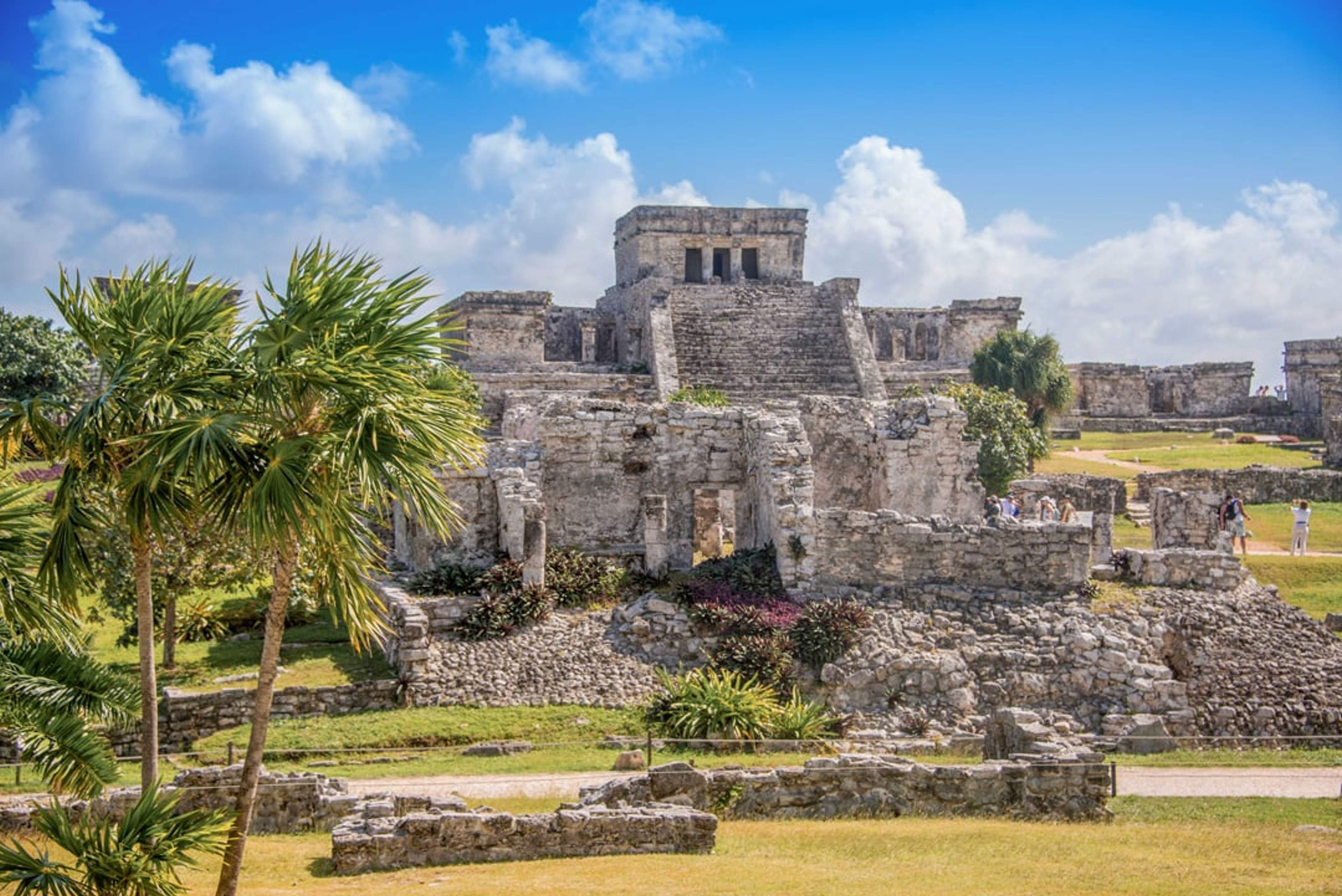 Antiguas ruinas mayas en Tulum, México, con un templo central y vegetación frondosa.