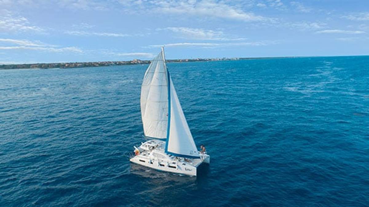 Velero deslizándose sobre las aguas azules de Cancún con la costa a lo lejos.