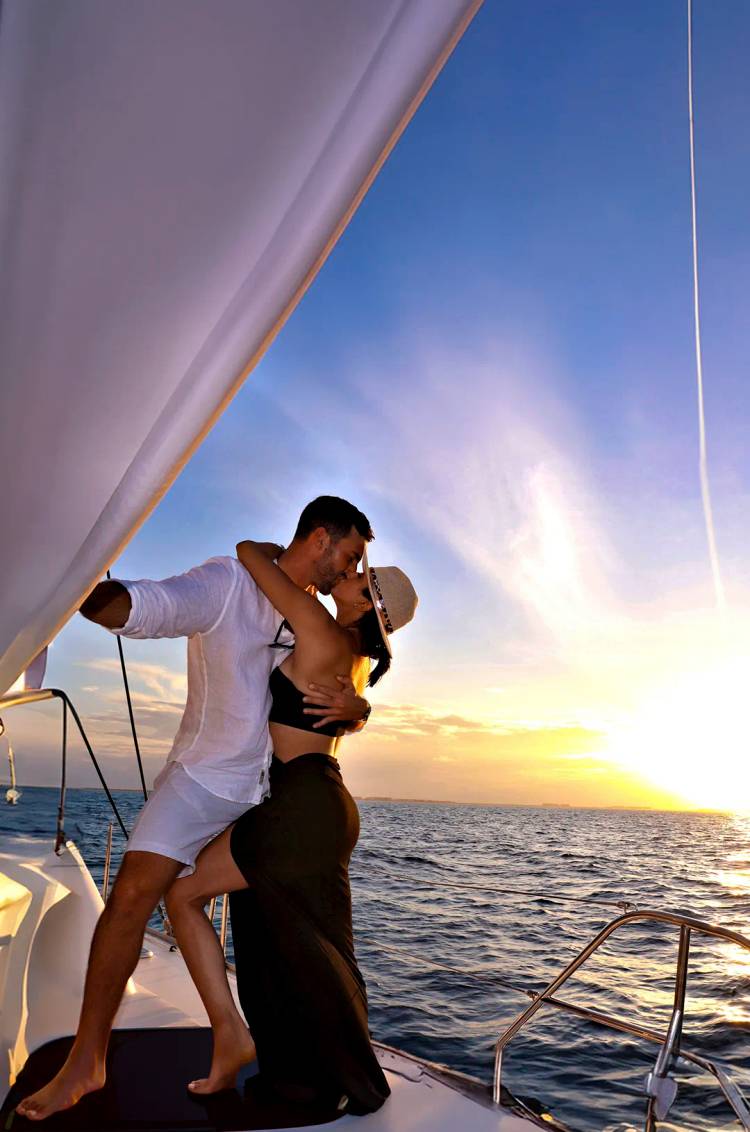 Una pareja se besa apasionadamente en un velero durante una hermosa puesta de sol en el océano.