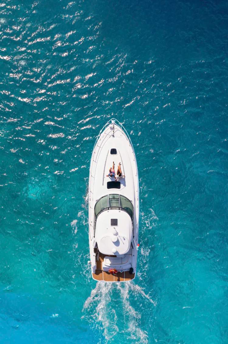 Aerial view of a luxury yacht cruising in turquoise waters, with two people relaxing on deck