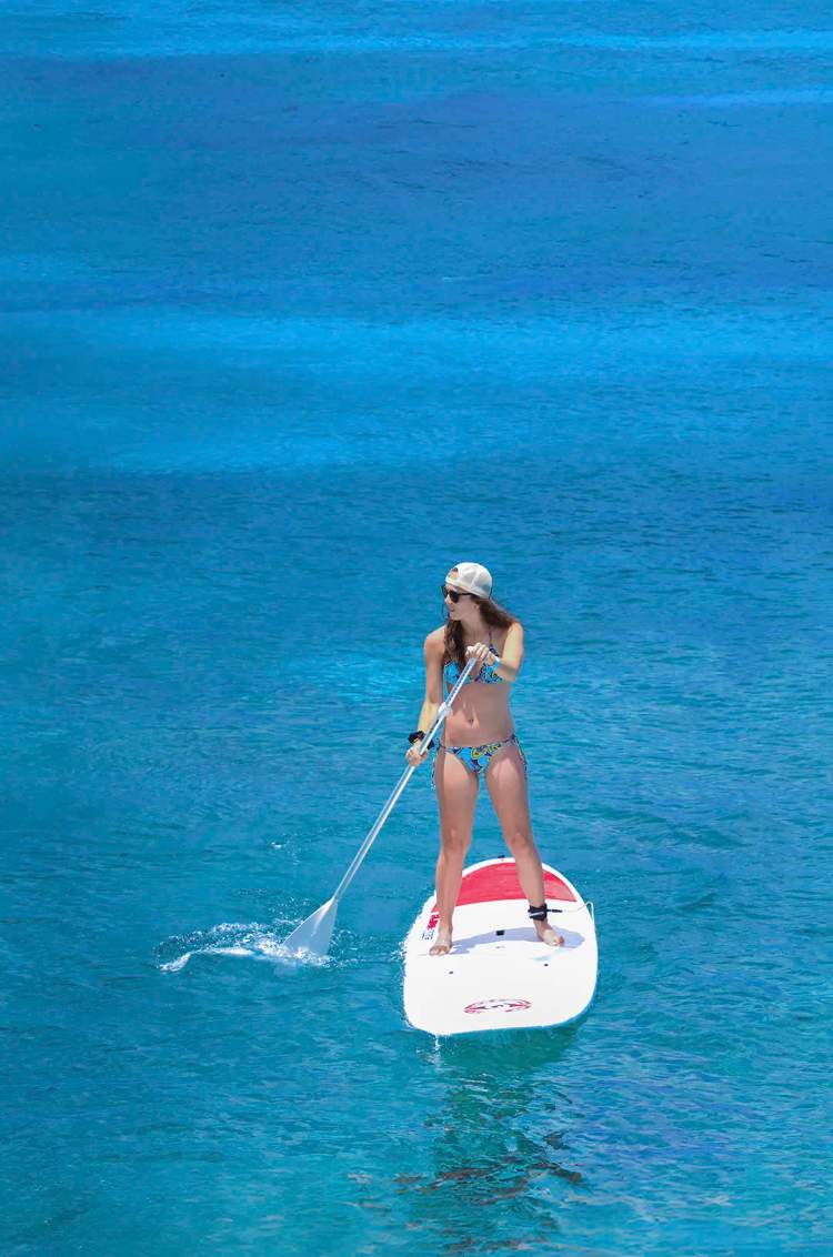 Woman paddleboarding in clear waters, enjoying a sunny day on the ocean.