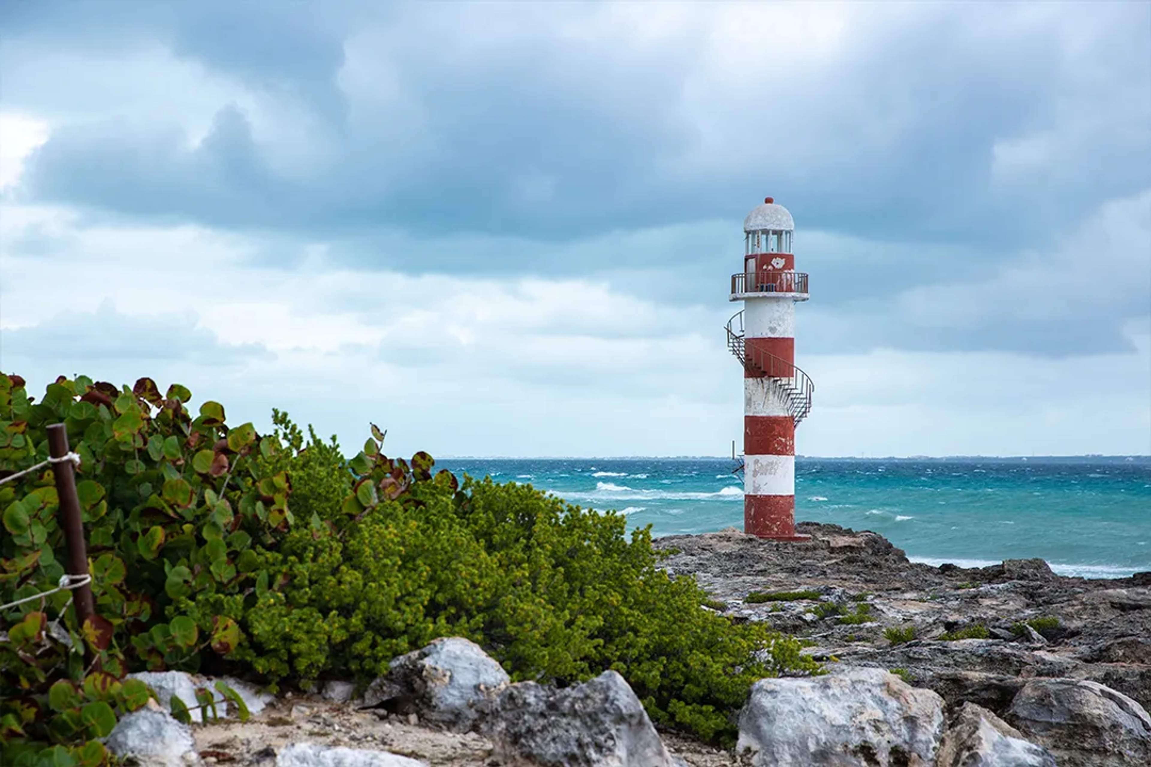 Striped lighthouse on rocky Caribbean coast under cloudy sky, Riviera Maya scenic coastal tour view