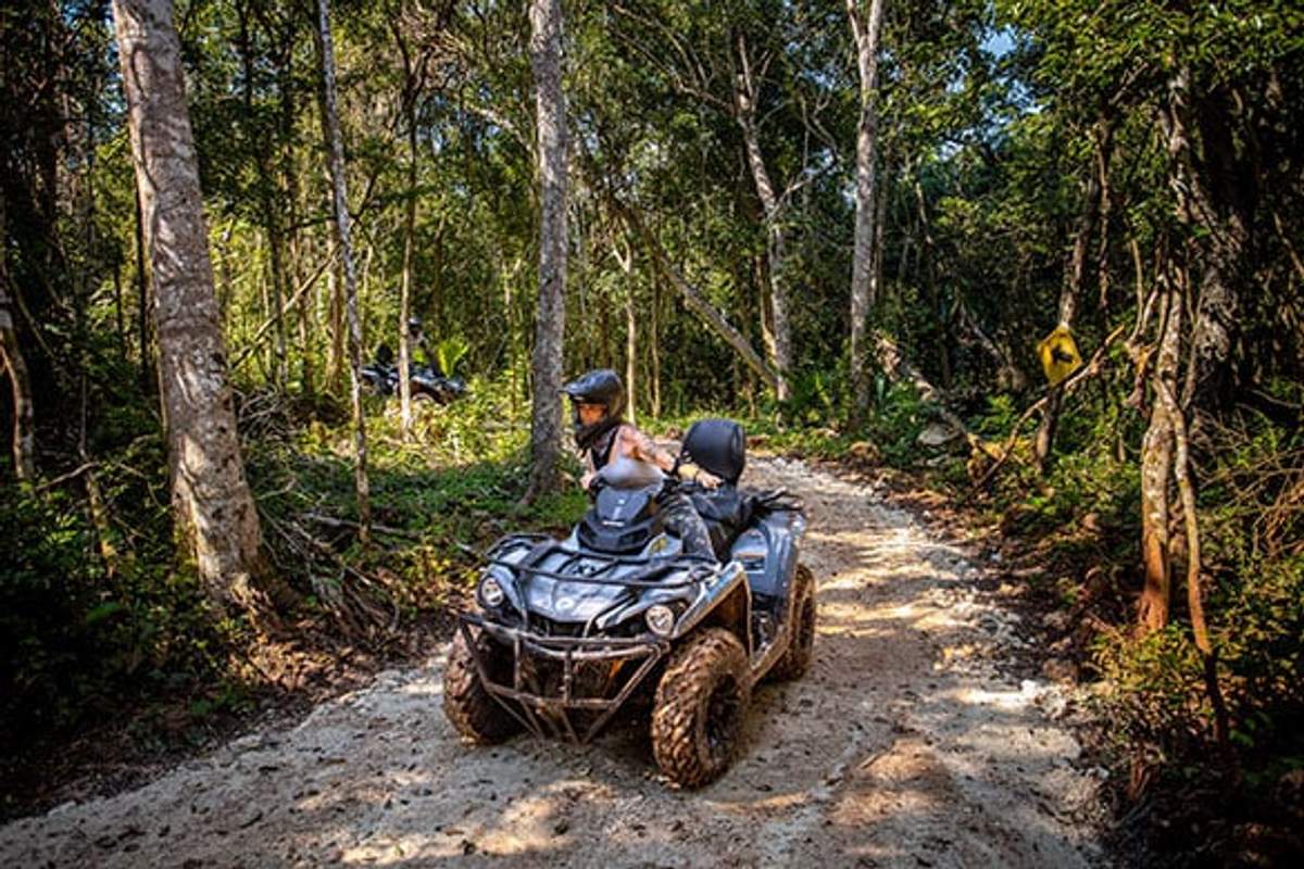 Una pareja conduciendo un ATV por un sendero en la selva de Cancún, rodeados de vegetación exuberante y disfrutando de una aventura.