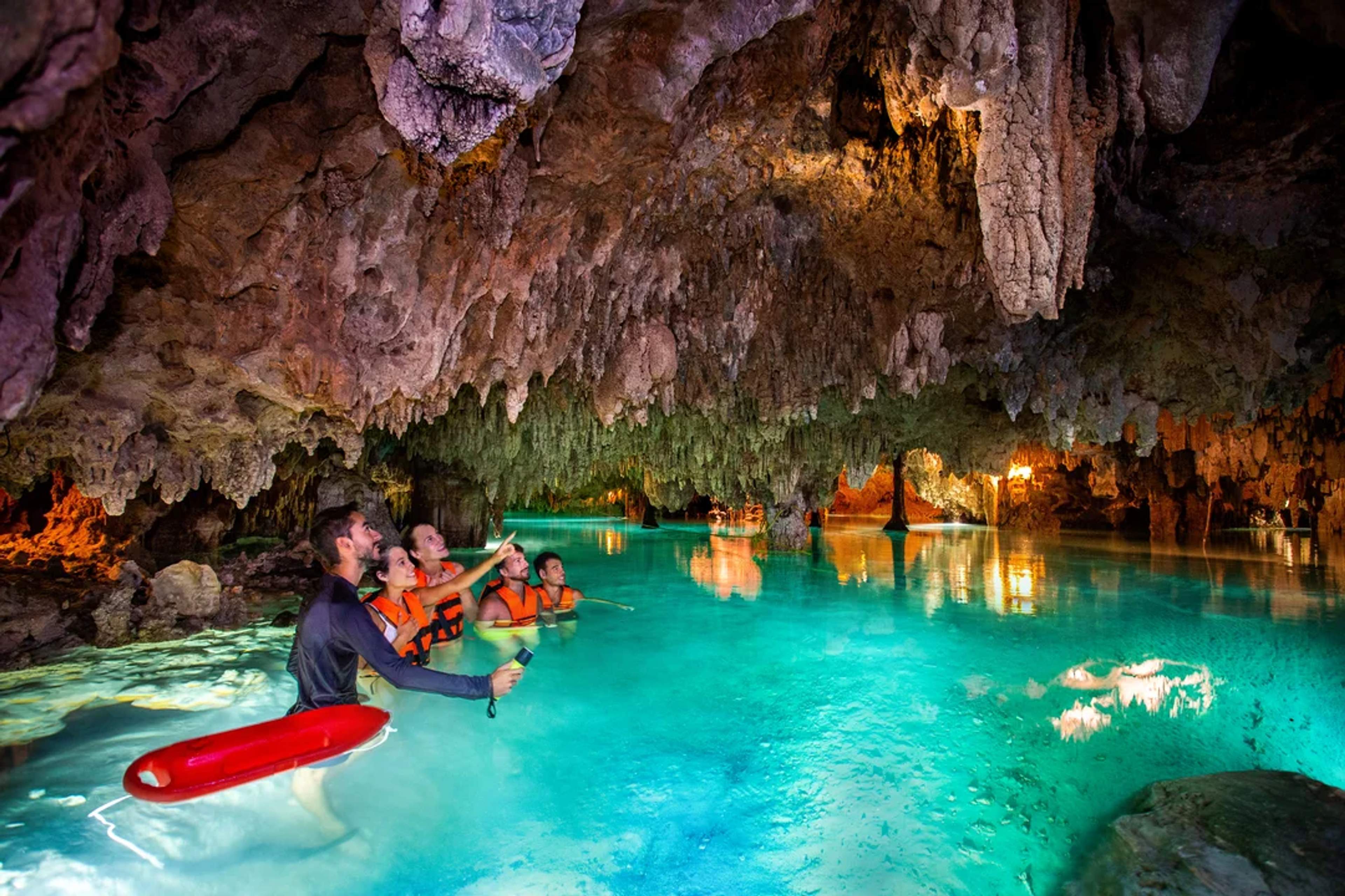Visitantes exploran un río subterráneo cristalino dentro de una cueva llena de estalactitas.