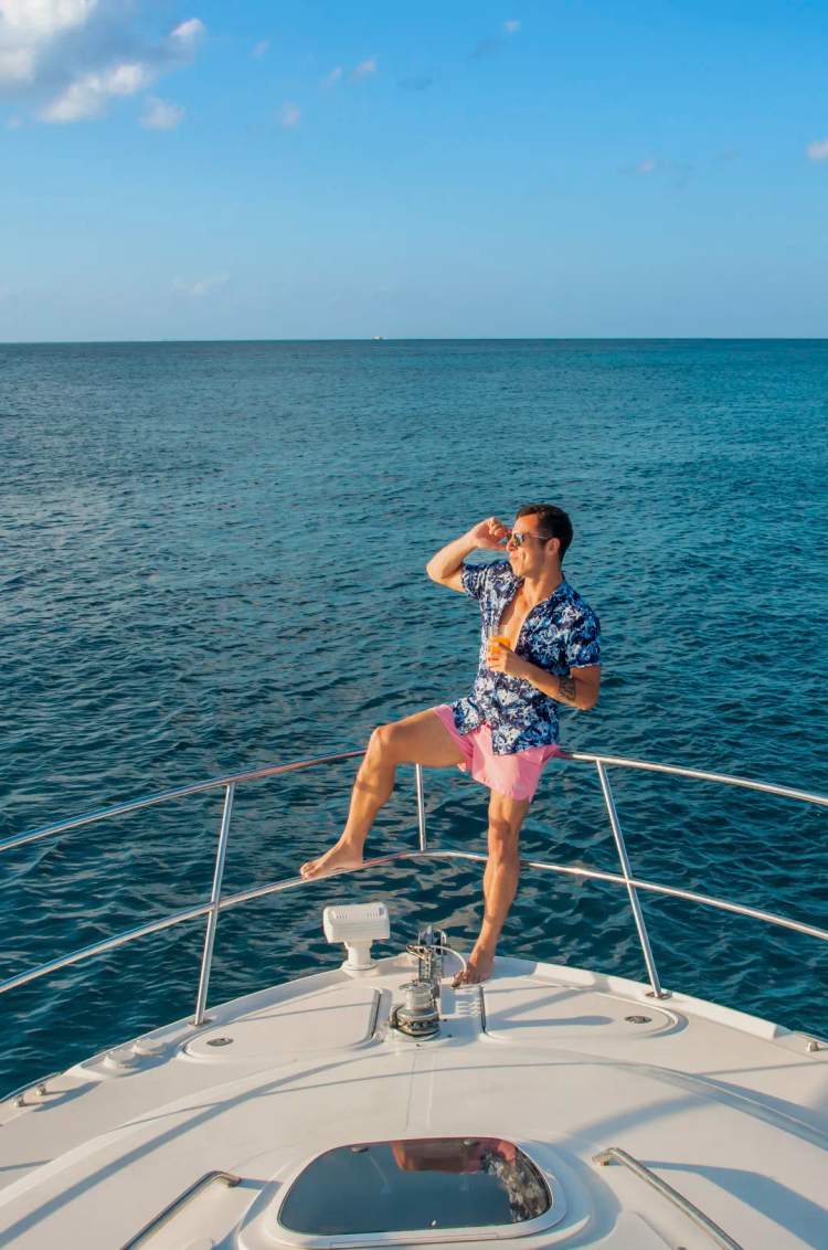 Man enjoying a drink on the bow of a yacht, gazing at the horizon on a sunny day.