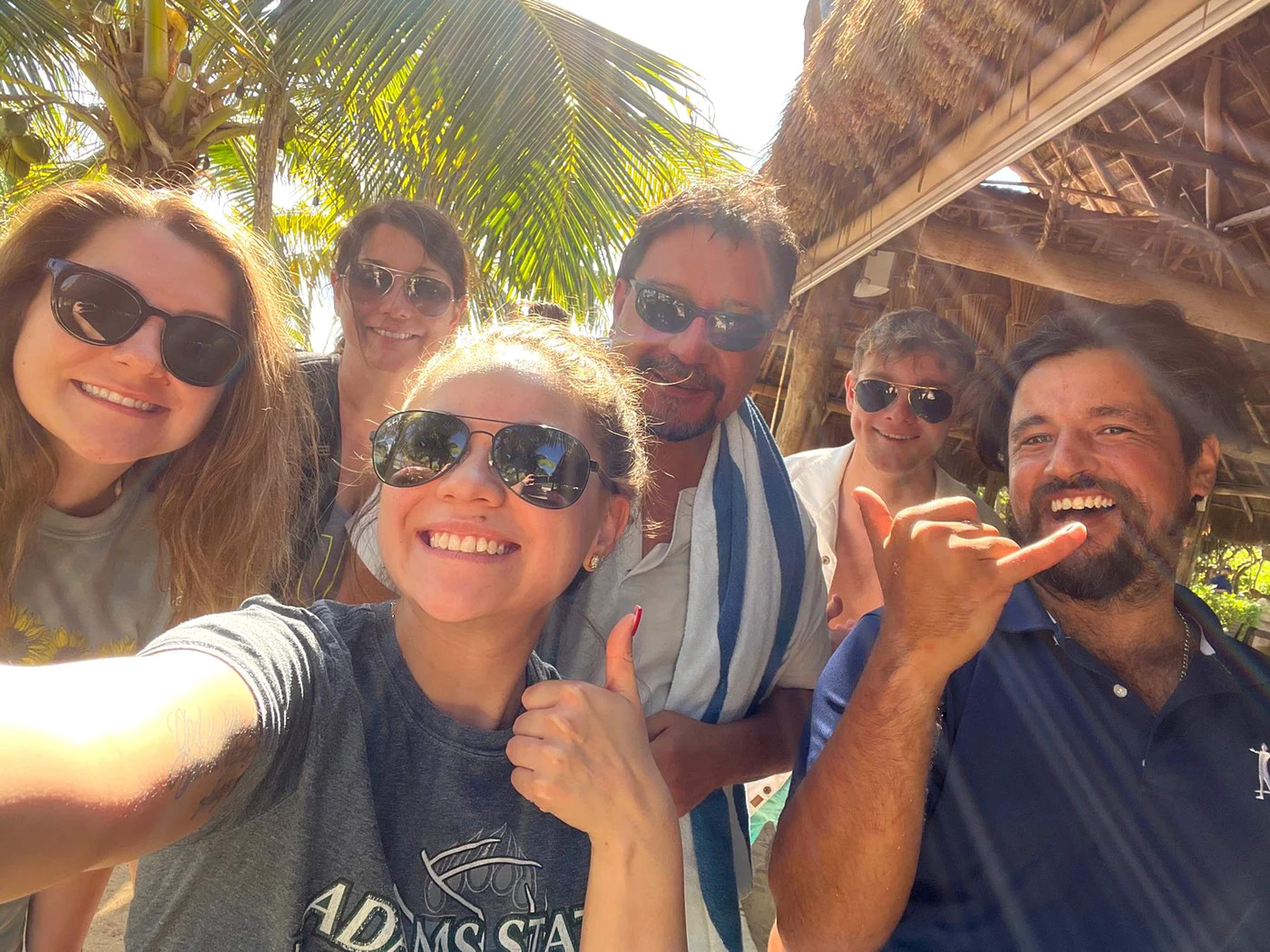 Grupo de amigos sonriendo y posando para una selfie en un bar de playa tropical en Cancún.