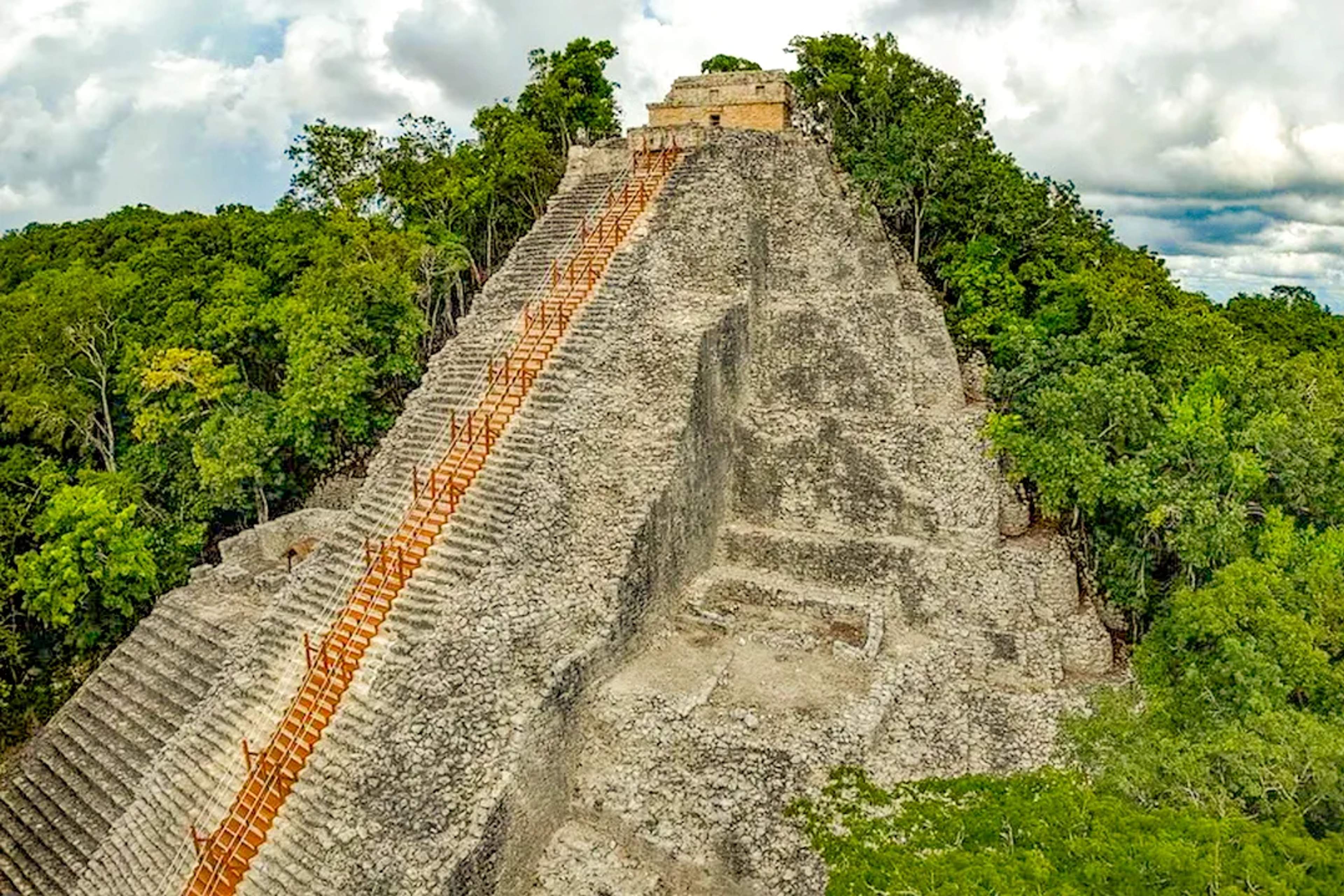 Pirámide maya de Cobá emergiendo sobre la selva, con empinadas escalinatas de piedra y exuberante vegetación tropical