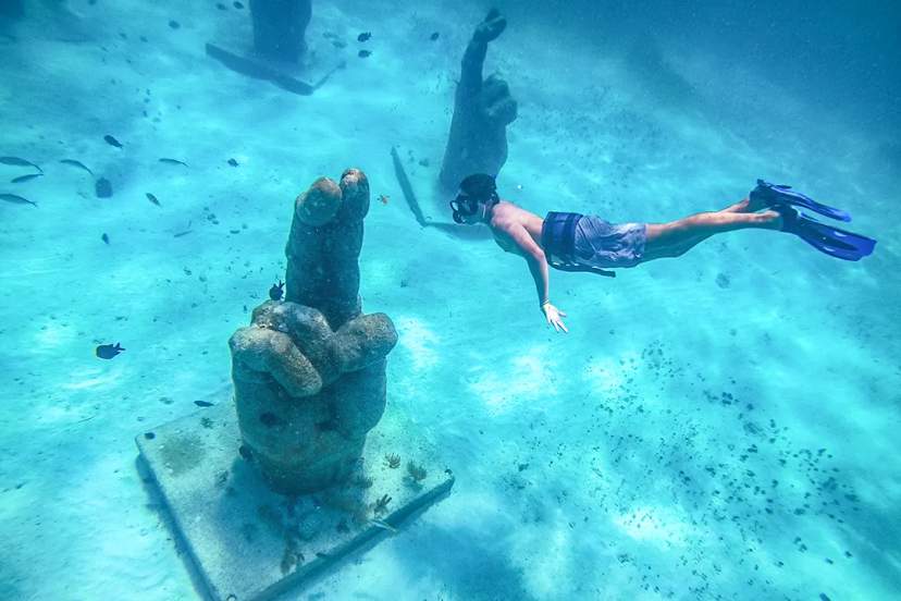 Snorkeler swimming over underwater sculptures surrounded by tropical fish in clear turquoise waters, Mexico