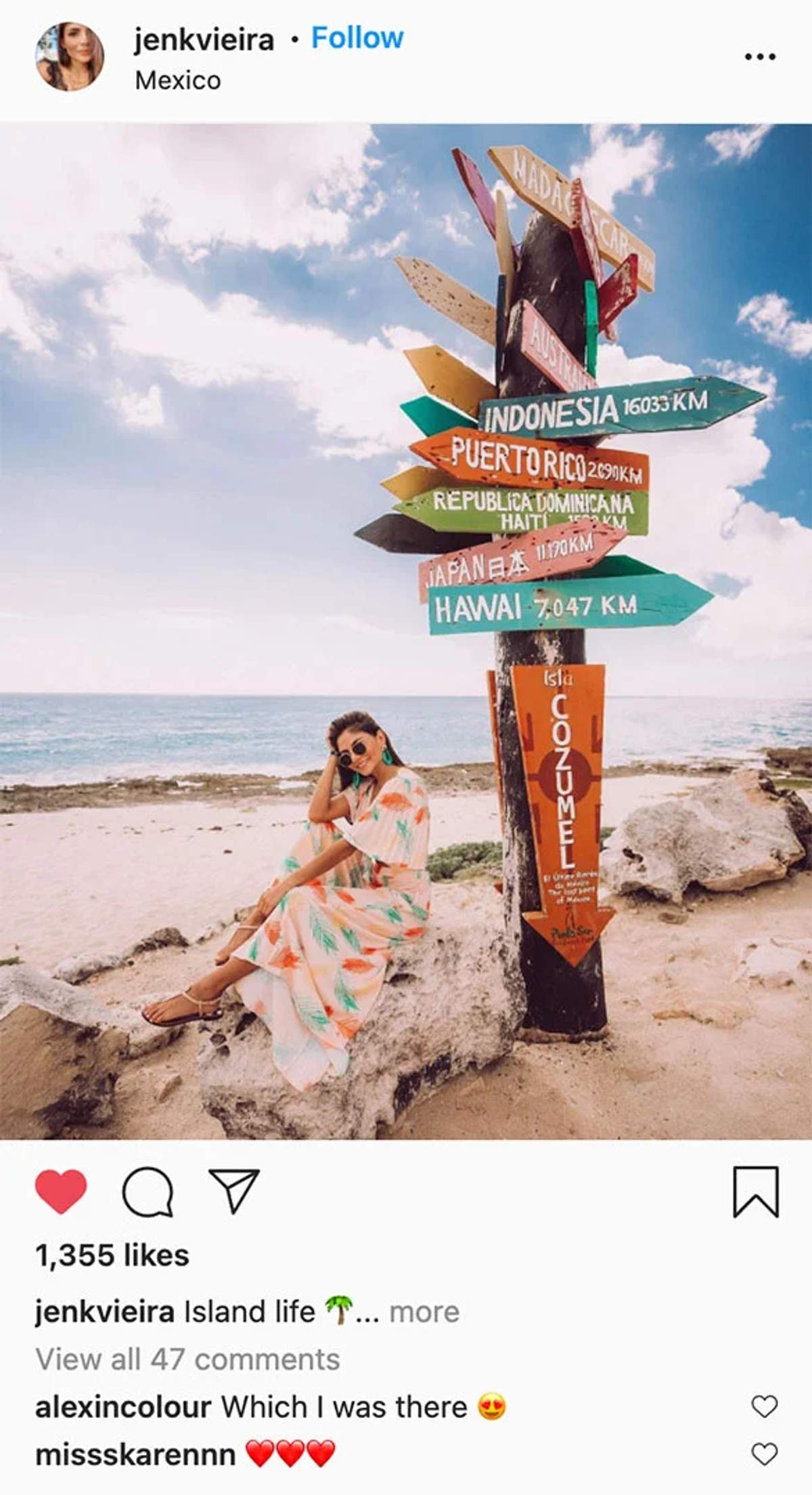 A woman sitting by a colorful signpost with arrows pointing to various destinations, on a beach in Cozumel.