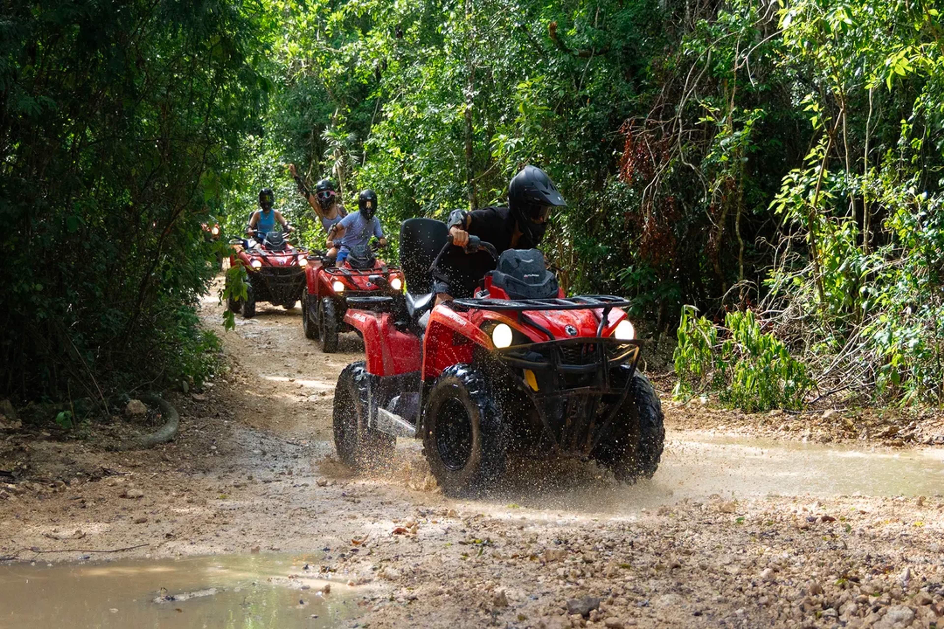 Aventureros recorren un sendero selvático en cuatrimotos, salpicando agua y disfrutando de la adrenalina.