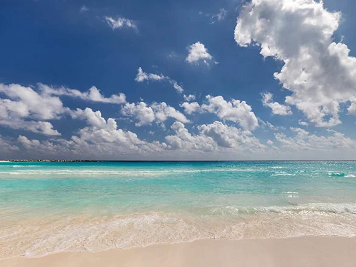 Cancun beach during hurricane season with clear turquoise waters and cloudy skies.