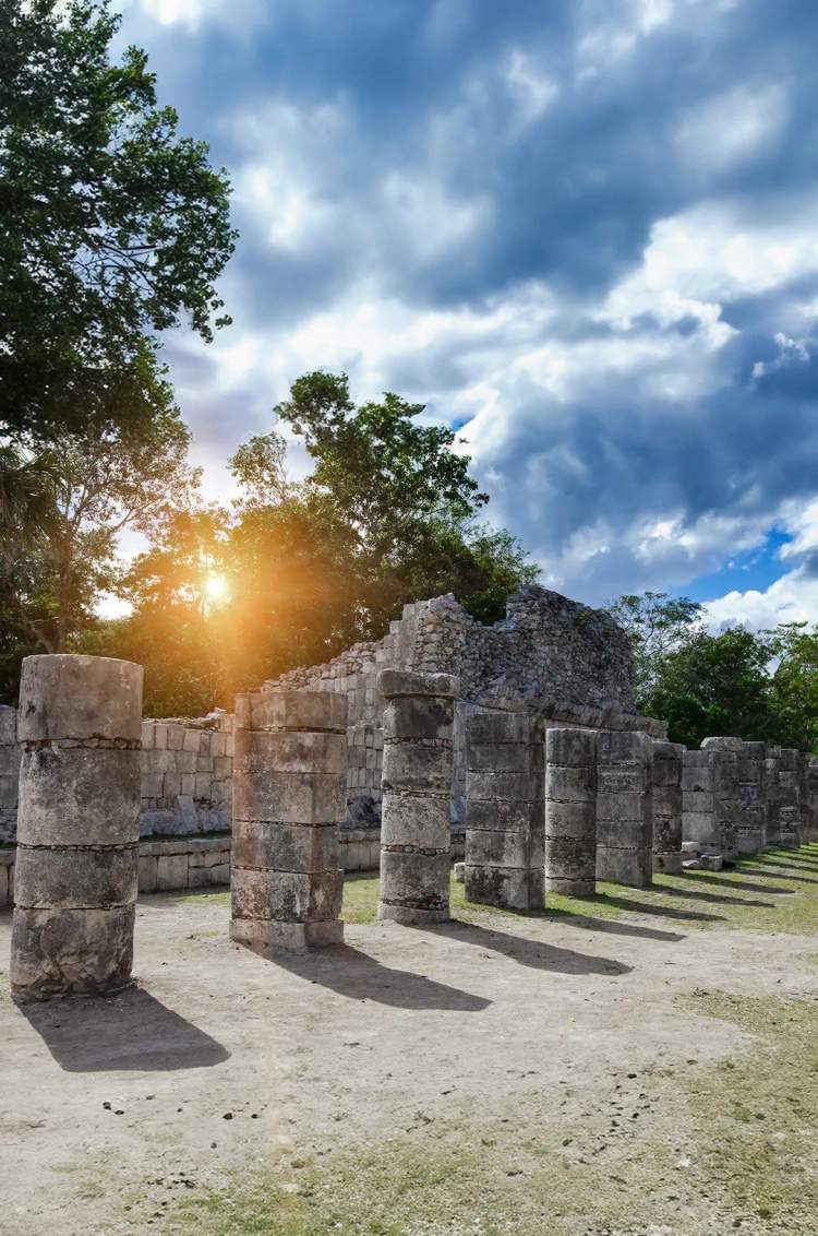 Ancient stone columns at Chichen Itza, bathed in sunlight, casting long shadows on the ground.