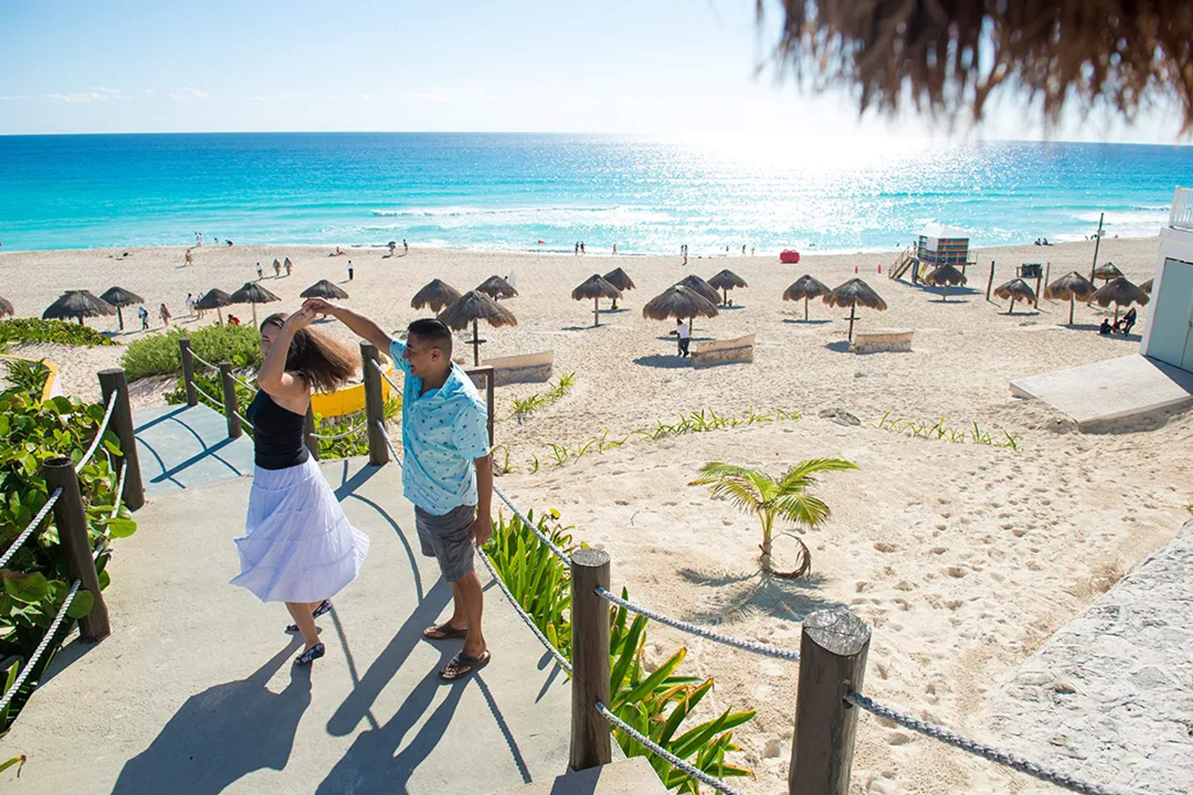 Couple at Playa Delfines beach with turquoise Caribbean views, white sand, and iconic Cancun sign oceanfront