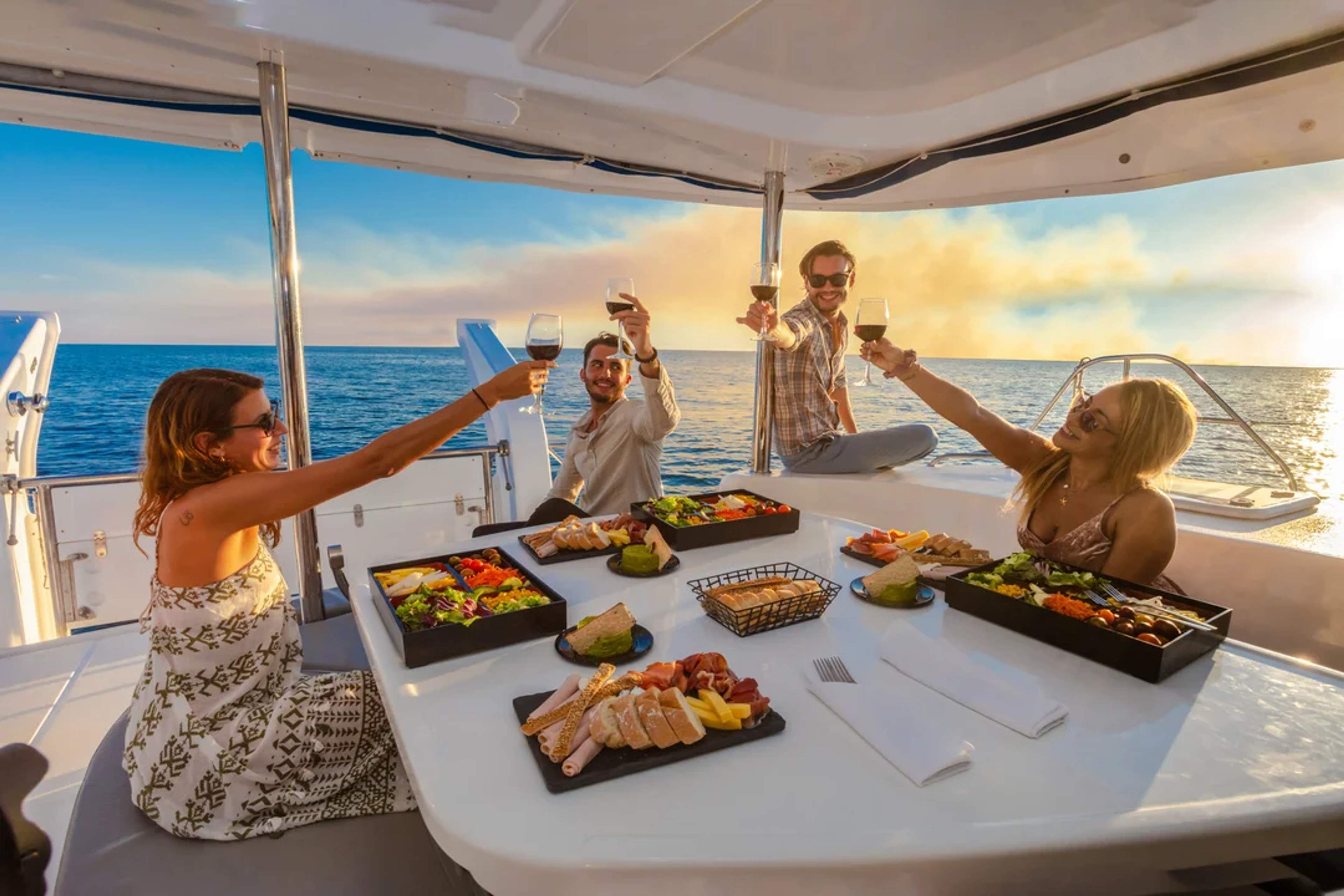 Brindis al atardecer en yate con amigos, vino y comida gourmet frente al mar.