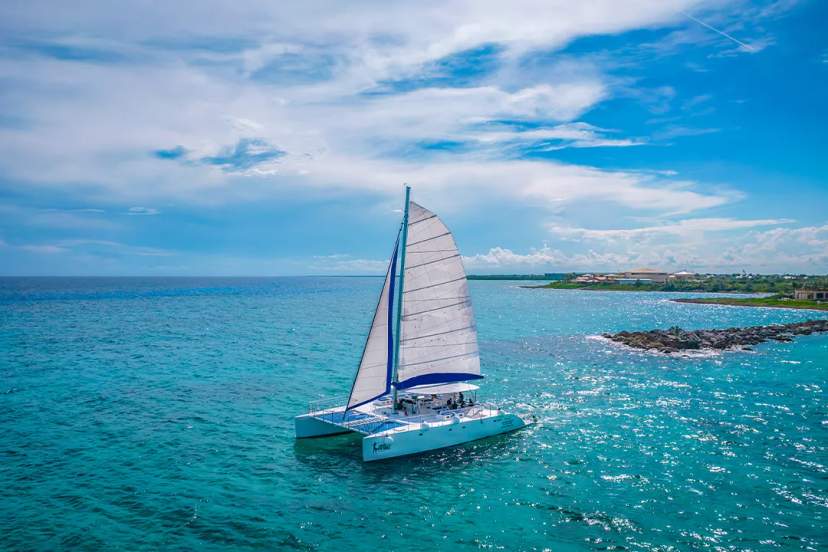 Catamarán navegando en las aguas azules de Cancún bajo un cielo despejado, cerca de la costa.
