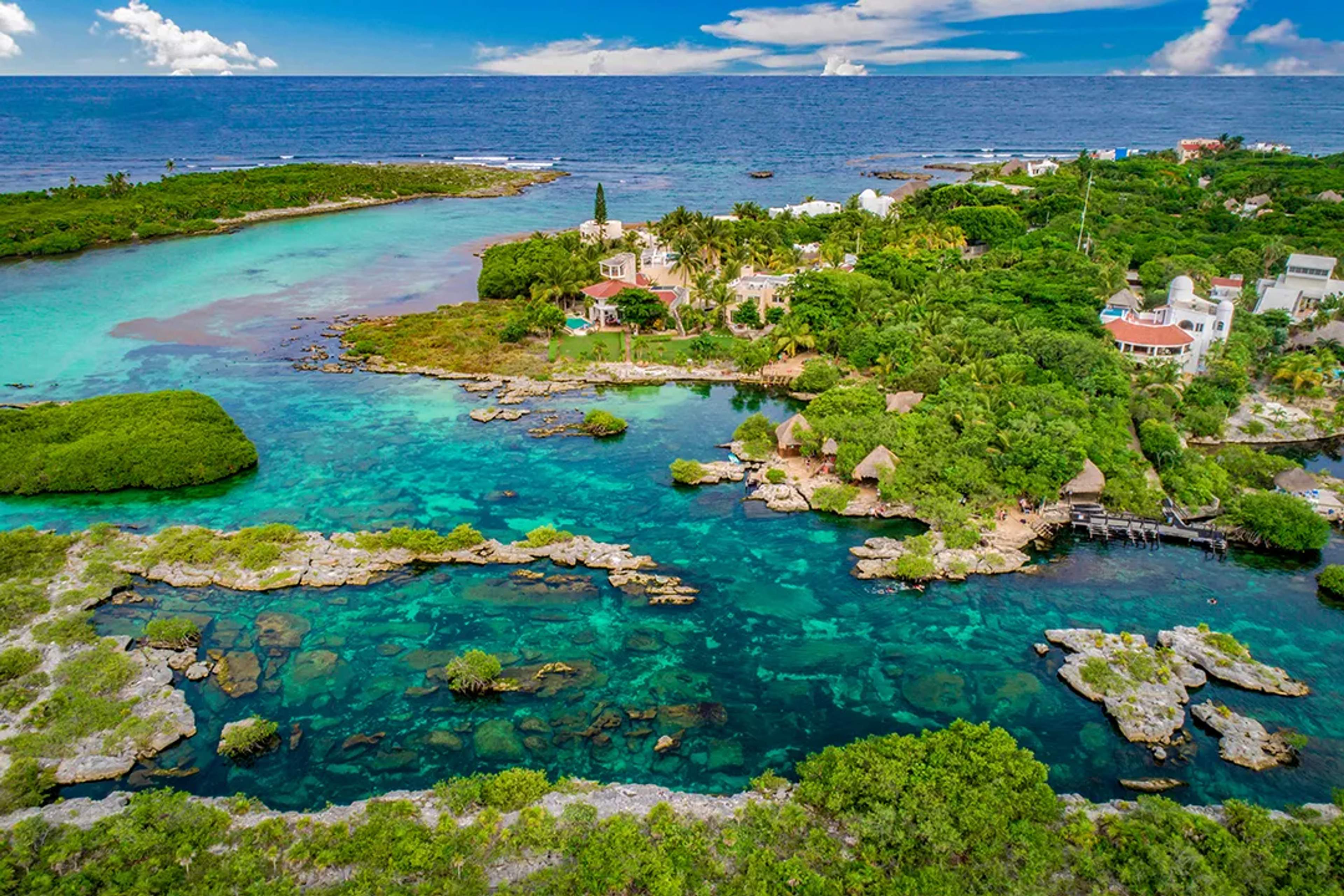 Vista aérea de una laguna tropical con aguas turquesa, vegetación y casas costeras.