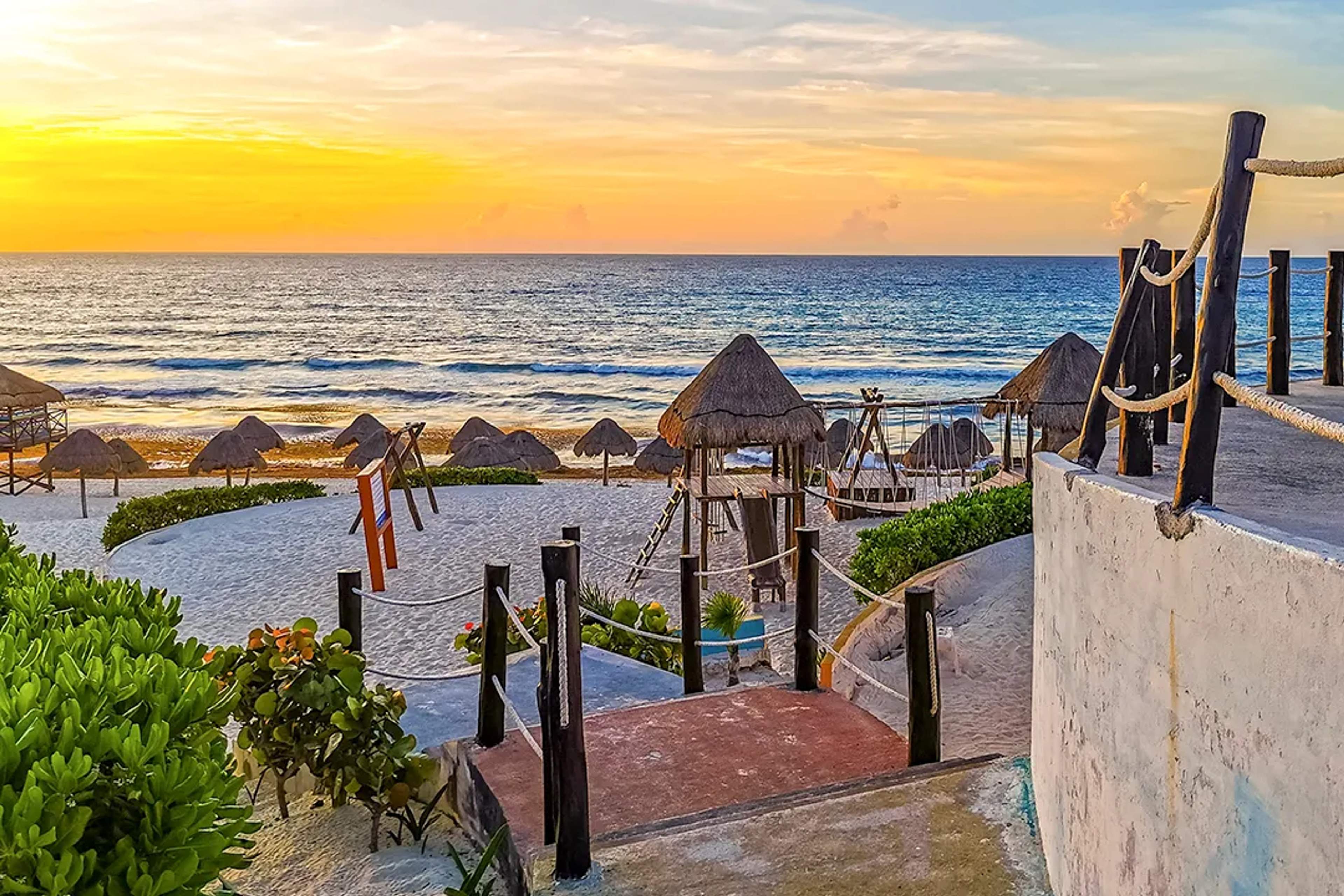 Atardecer en Playa Delfines Cancún con olas del Caribe, playa de arena blanca y palapas frente al mar