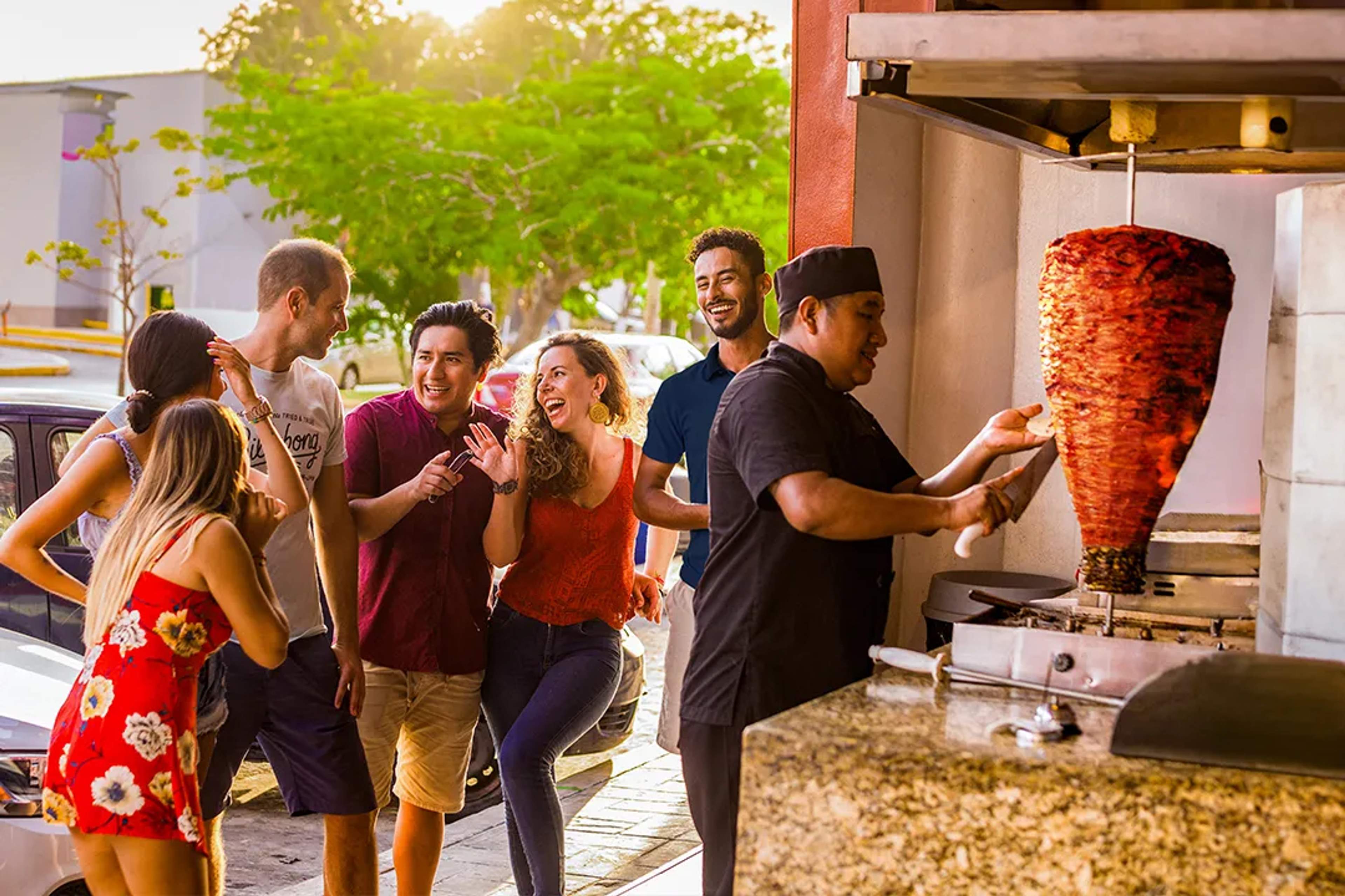 Friends laughing together while enjoying street tacos al pastor in Playa del Carme.