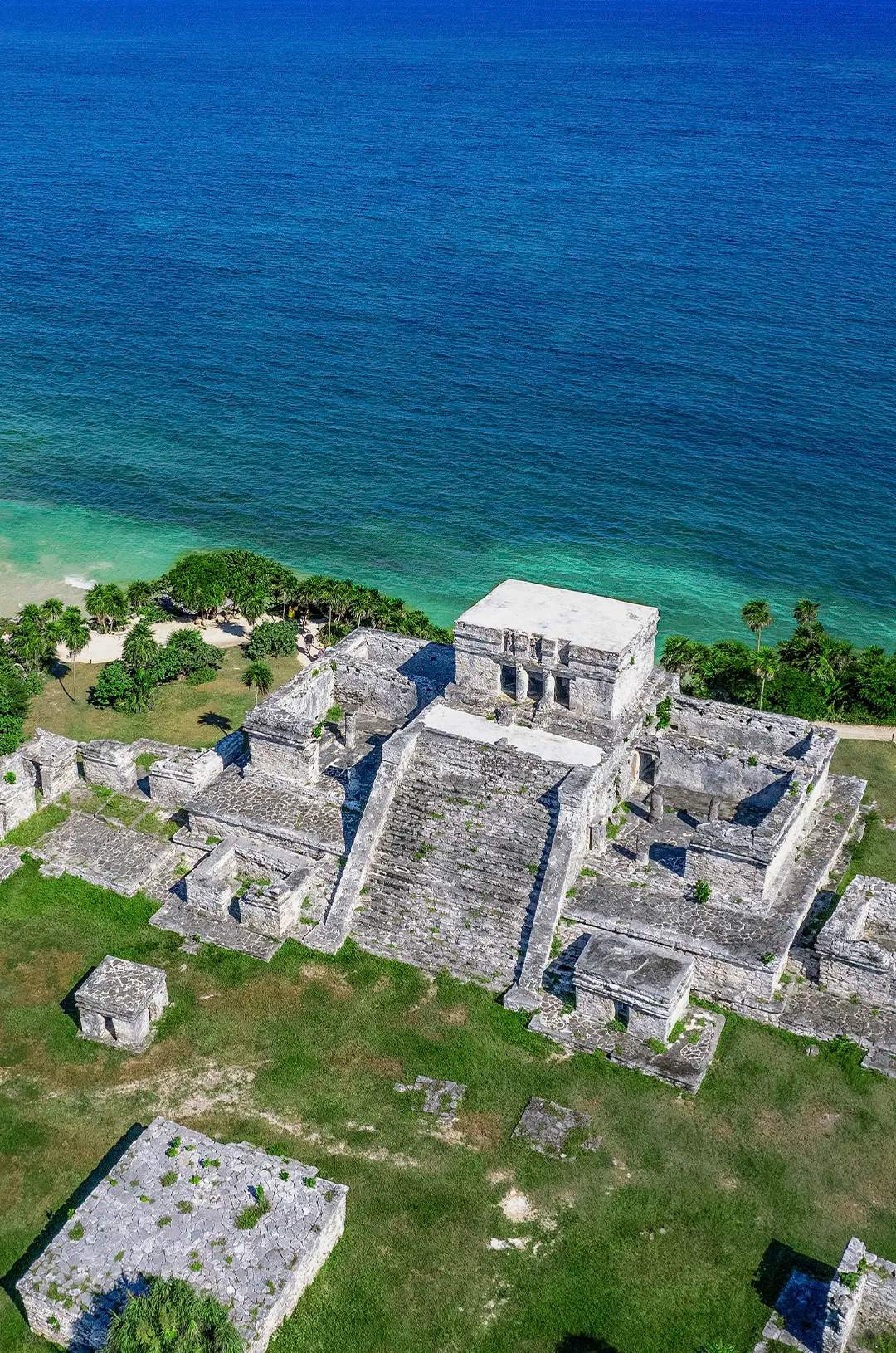 Aerial view of the Mayan ruins of Tulum on a cliff overlooking the Caribbean Sea. The site features stone structures.