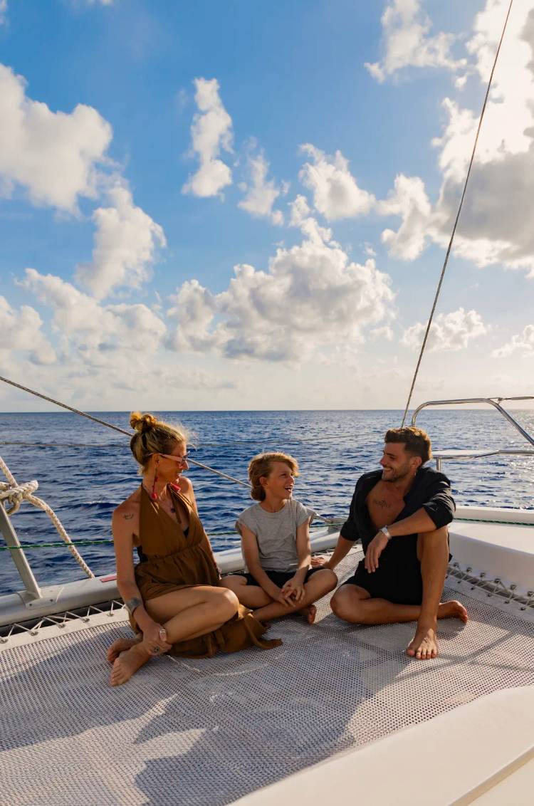 Una familia disfruta de un día soleado navegando en un barco, sentados y sonriendo en la cubierta con el océano de fondo.