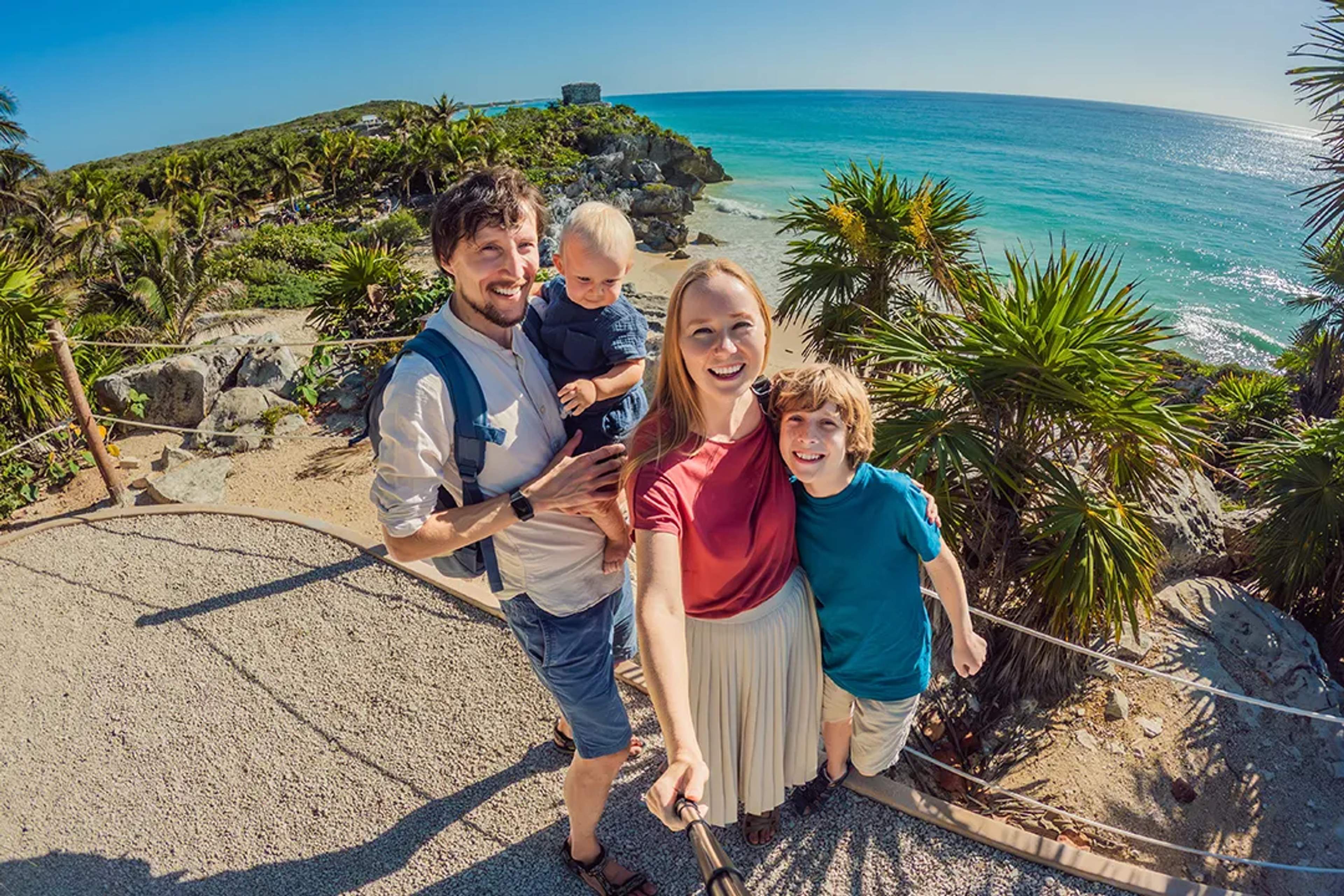 Family enjoying a scenic viewpoint in Tulum, Mexico, with turquoise Caribbean Sea, palm trees, and ancient ruins
