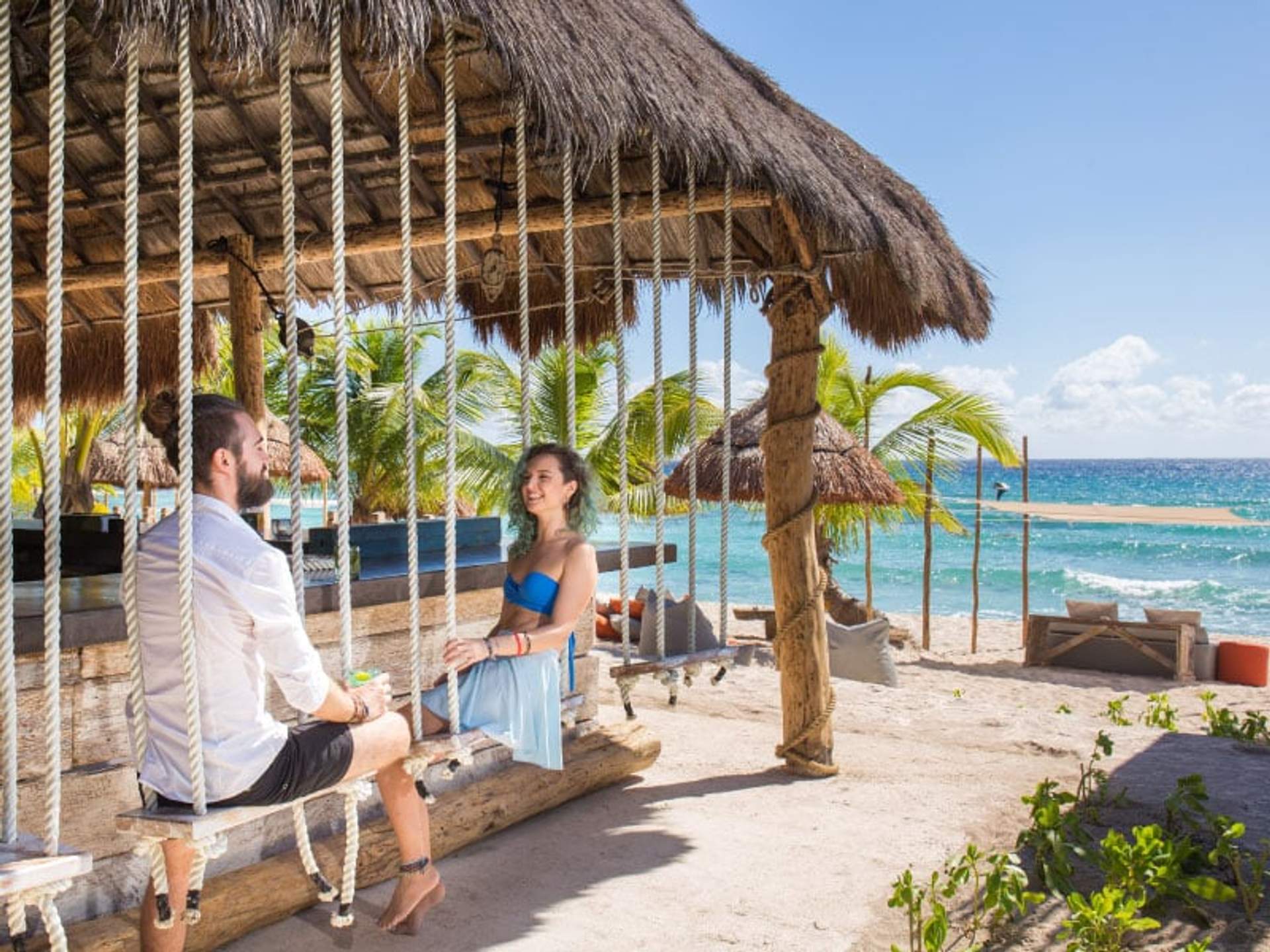 Couple on swings at a beach club in Cancun, enjoying drinks and ocean view.