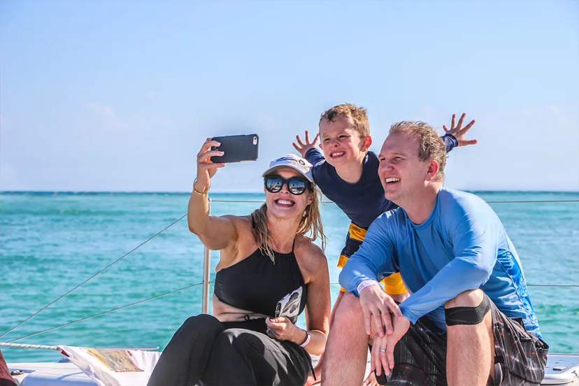 Family taking selfie on Cancun catamaran tour with turquoise Caribbean Sea and sunny tropical views