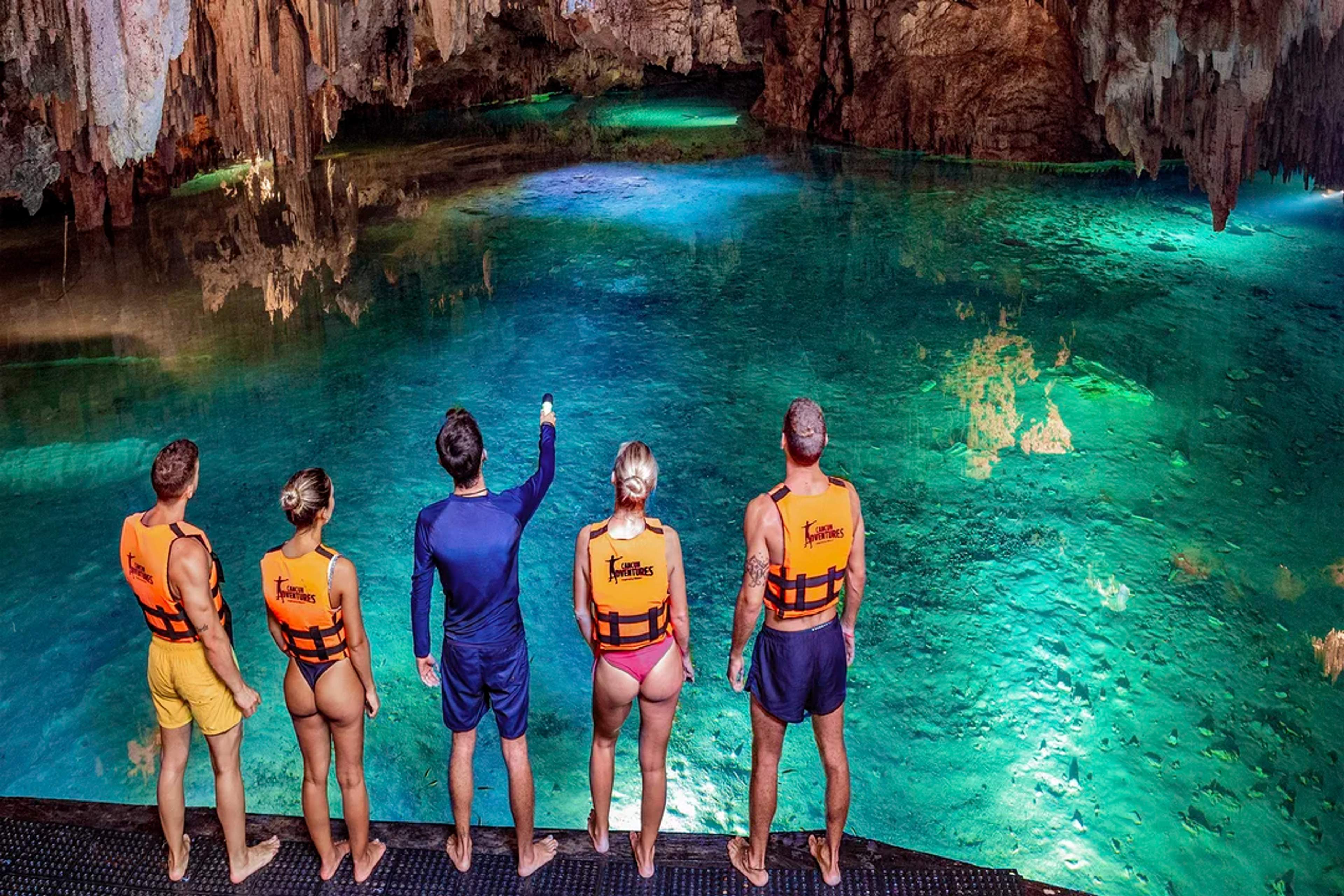 Un grupo se encuentra al borde de un impresionante cenote, admirando sus aguas cristalinas y su mágica belleza subterránea.