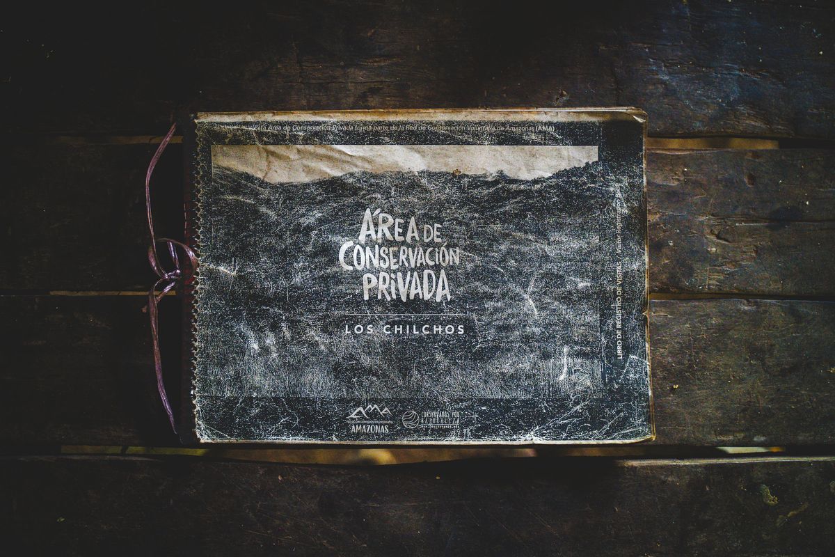 Worn cover of the visitor registry book for the Chilchos Private Conservation Area, lying on a dark wooden table at the lodge