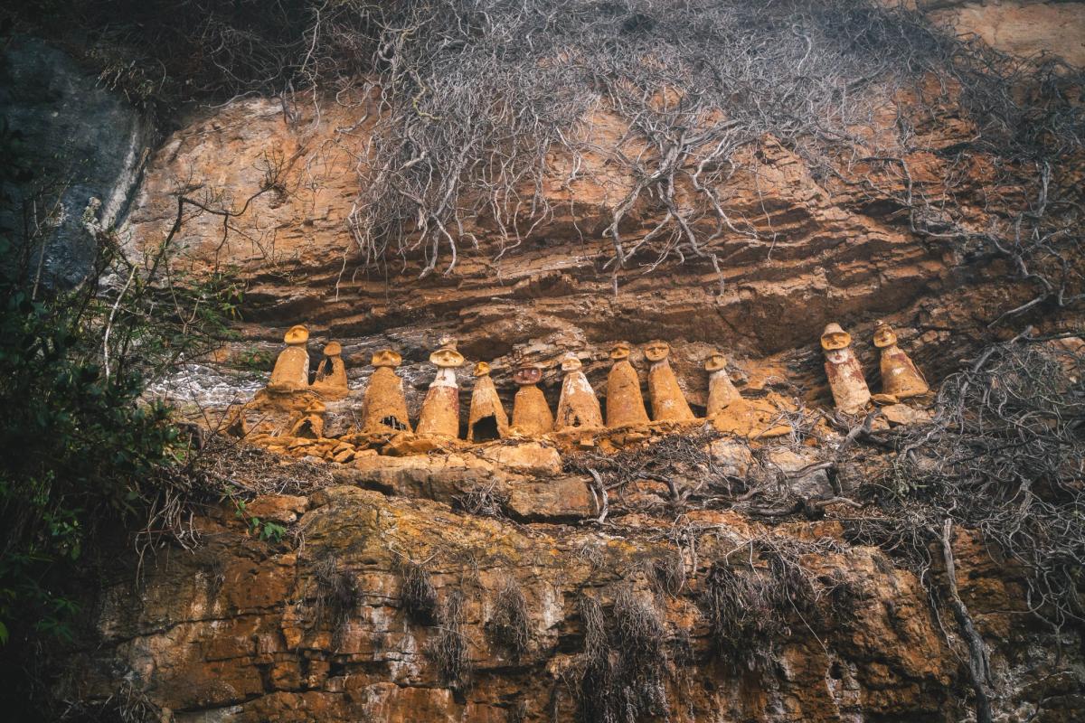 A row of Chachapoya sarcophagi with modeled faces and headdresses standing on a cliff ledge at Cerro el Tigre, San Jerónimo, Amazonas, Peru