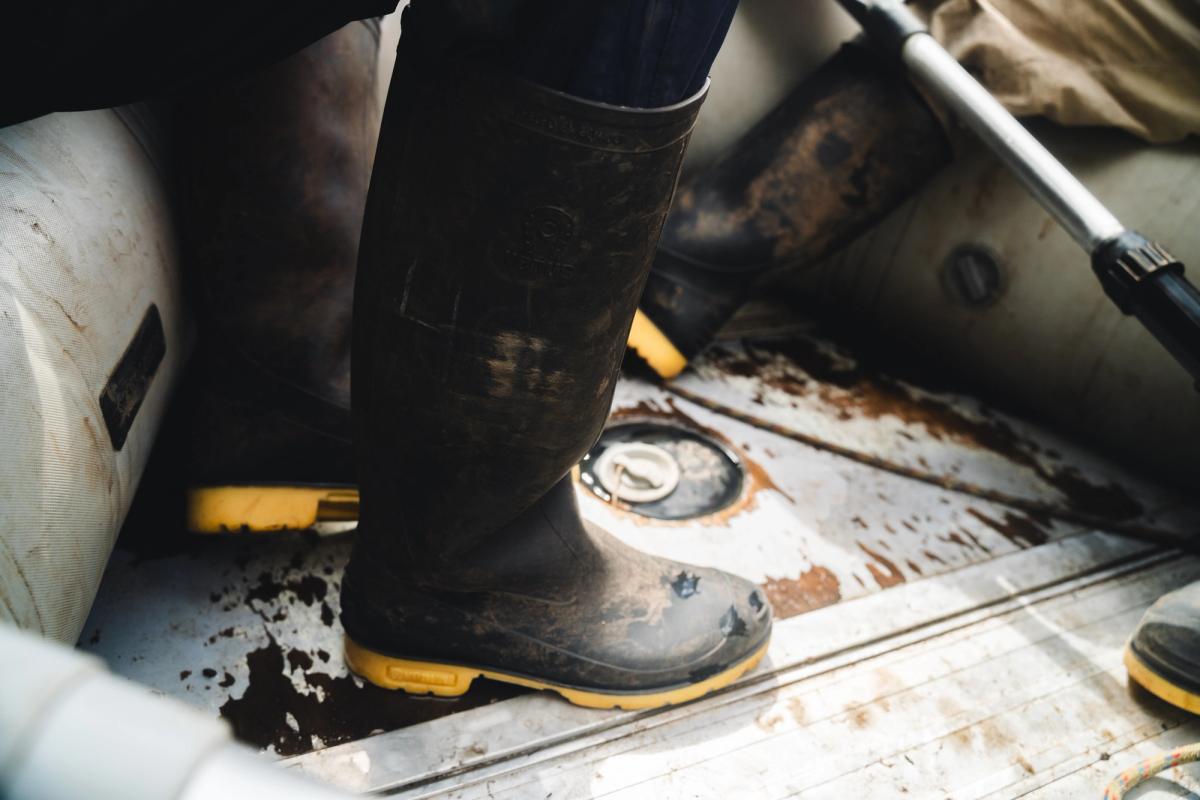 Muddy rubber boots resting on the wet floor of an inflatable boat beside a paddle, during the crossing of Laguna de los Cóndores