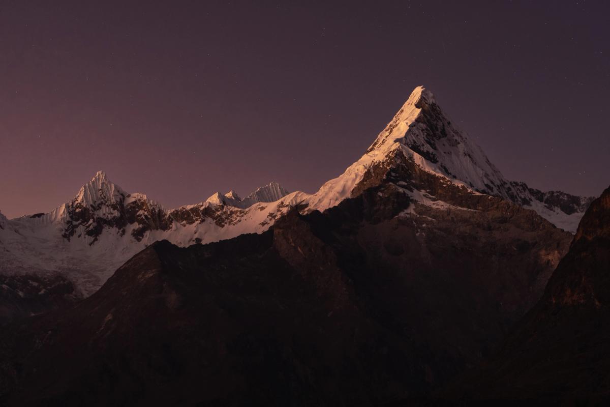 Sunrise over Nevado Artensonraju in the Peruvian Andes, with clear skies and soft blue and purple light illuminating the glaciated peak.