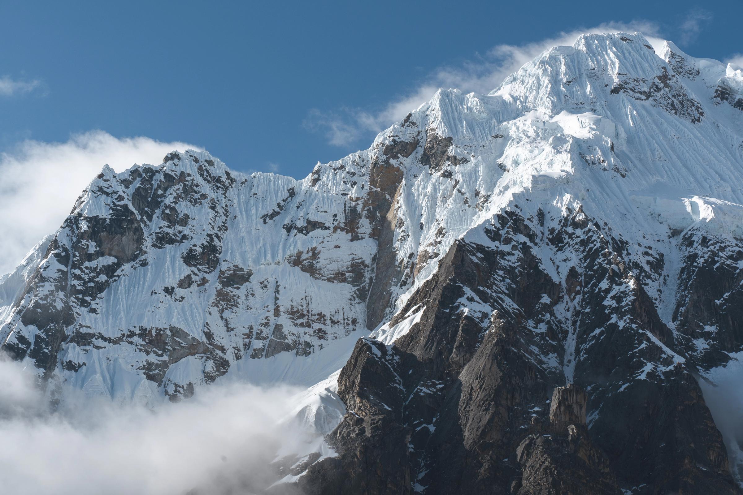 El Nevado Salkantay elevándose sobre los Andes, con sus empinadas laderas cubiertas de nieve y oscuras paredes rocosas dominando la ruta del popular Trek Salkantay hacia Machu Picchu bajo un cielo azul despejado.