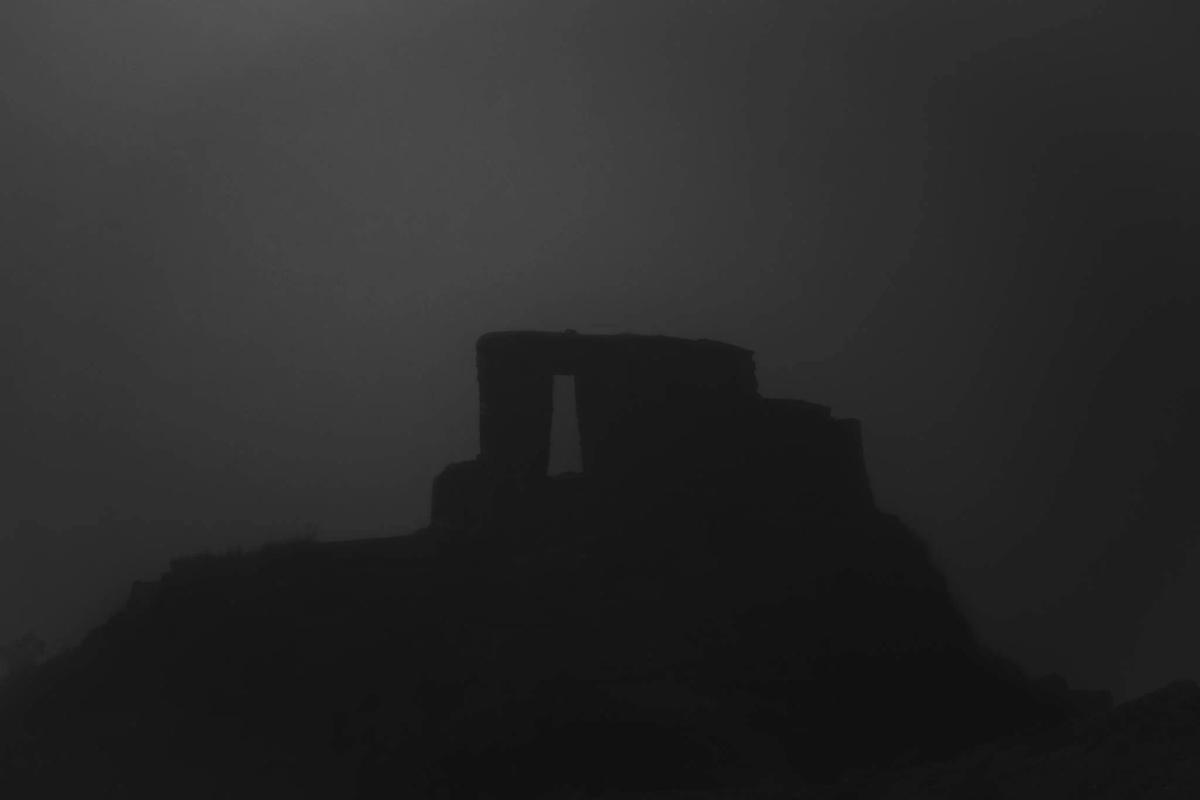 Silueta en blanco y negro de la portada inca de Inti Punku sobre su cresta encima de Ollantaytambo, envuelta en una densa neblina