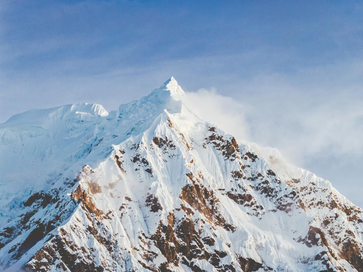 Vista aérea con dron de la pirámide nevada de la cumbre del Nevado Salkantay, con nieve volando desde la arista contra un cielo azul, vista desde la Casa del Montañista en el valle de Ahobamba, Perú