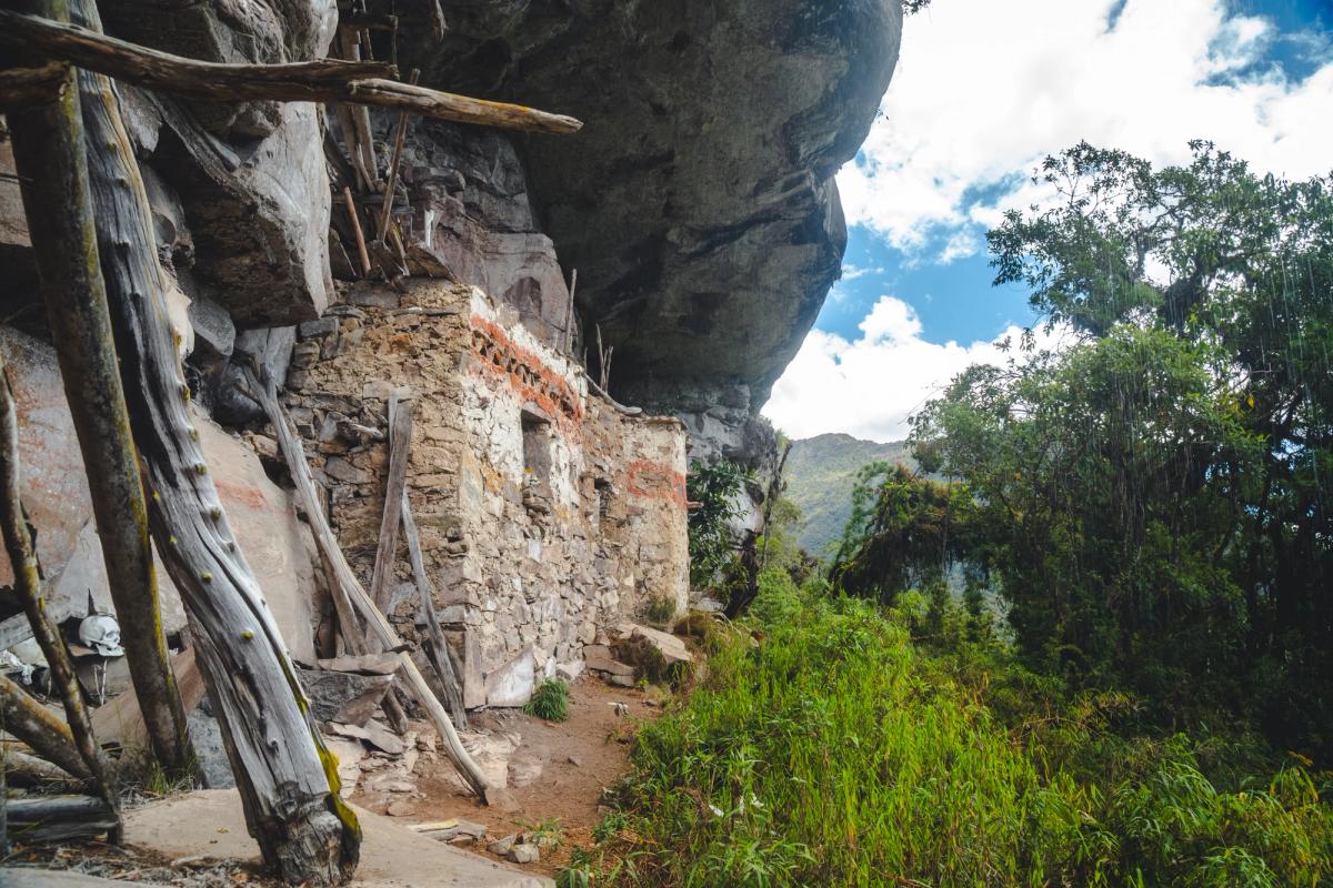 Chachapoya mausoleums built beneath a rock overhang, with red and white pigment on the walls, wooden beams, and a human skull among the remains