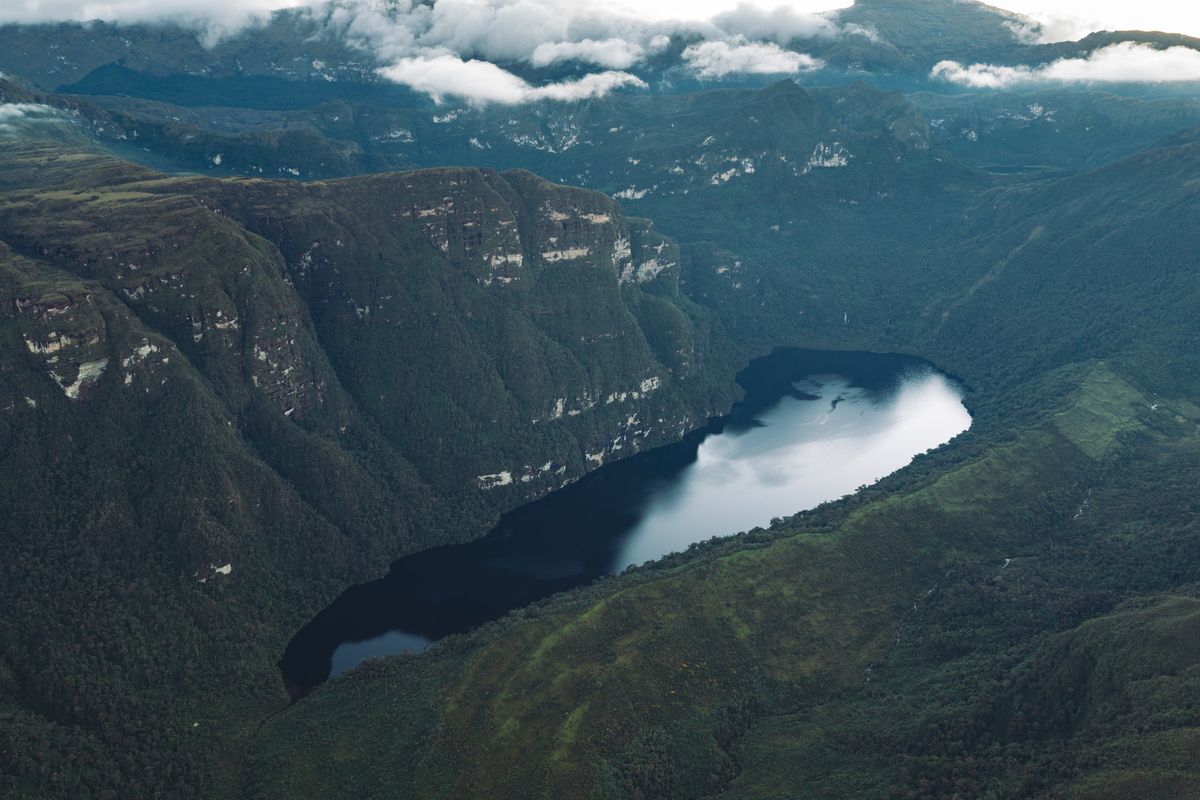 Aerial view of Laguna de los Cóndores, its dark water surrounded by cliff bands and dense cloud forest in the Amazonas region of Peru