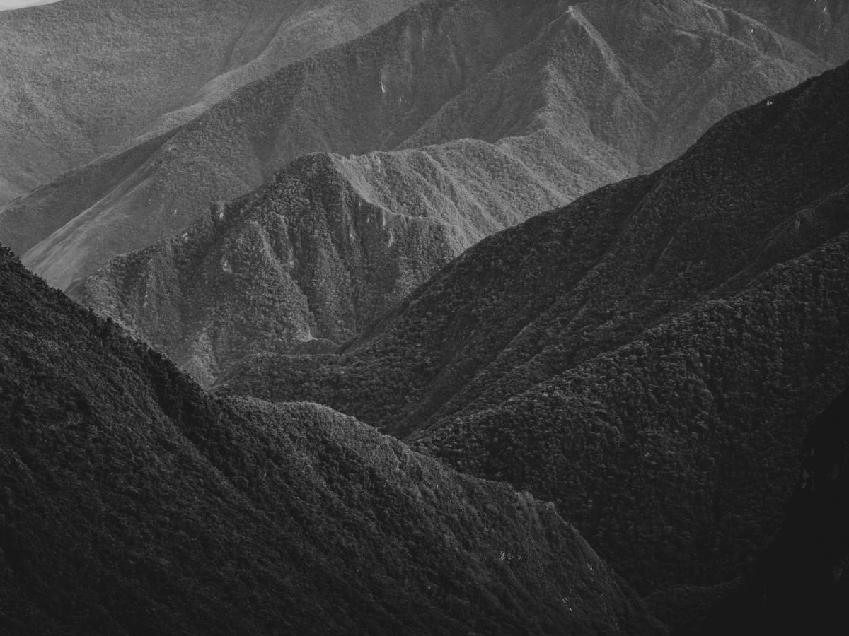 Vista aérea en blanco y negro, tomada con dron, del valle de Ahobamba hacia Machu Picchu, con capas de cerros cubiertos de bosque nuboso denso que se pierden en la distancia, región Cusco, Perú
