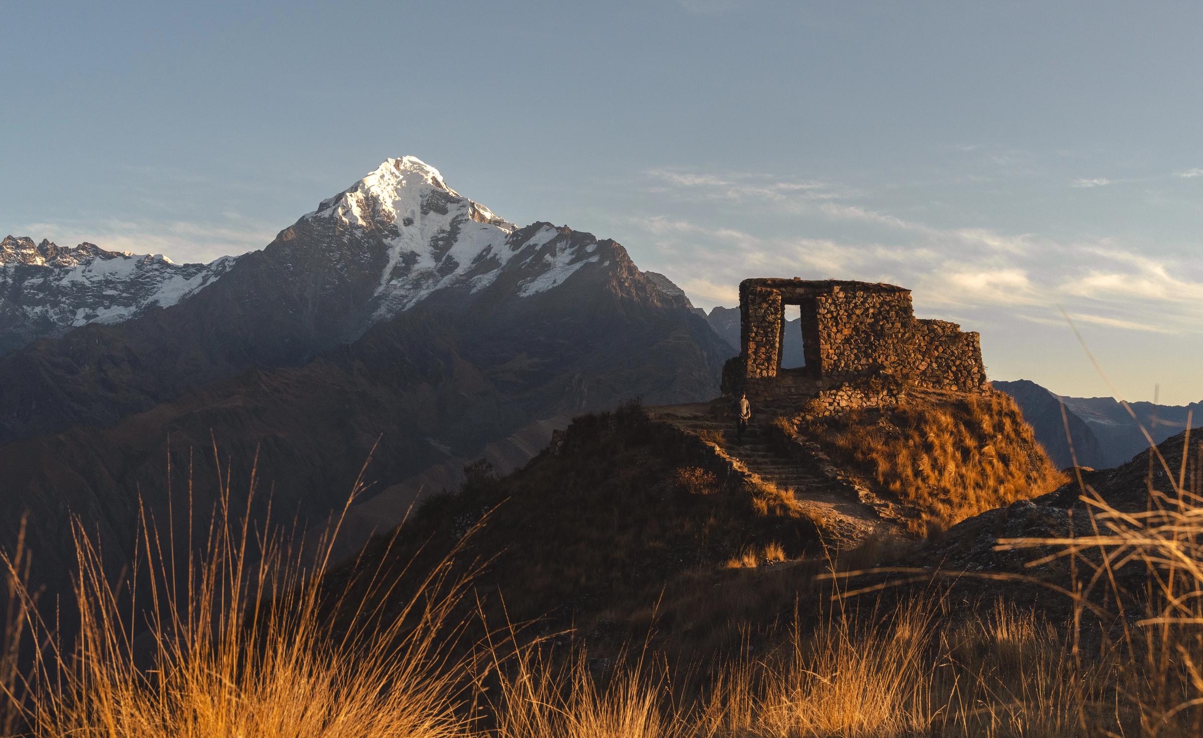 Un excursionista sube por el camino hacia la portada inca de Inti Punku sobre Ollantaytambo, con el Nevado Verónica detrás