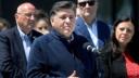 Illinois Governor JB Pritzker speaks at a microphone during a press conference with other officials standing behind him.