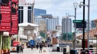 People walking along the Atlantic City boardwalk with casino hotels like Hard Rock in the background.