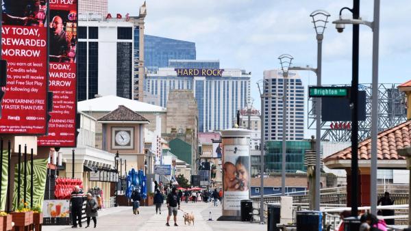 People walking along the Atlantic City boardwalk with casino hotels like Hard Rock in the background.