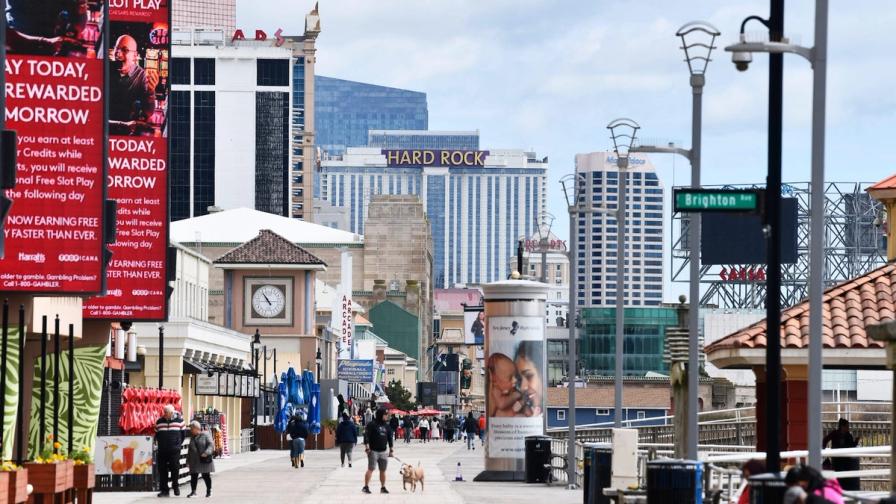 People walking along the Atlantic City boardwalk with casino hotels like Hard Rock in the background.